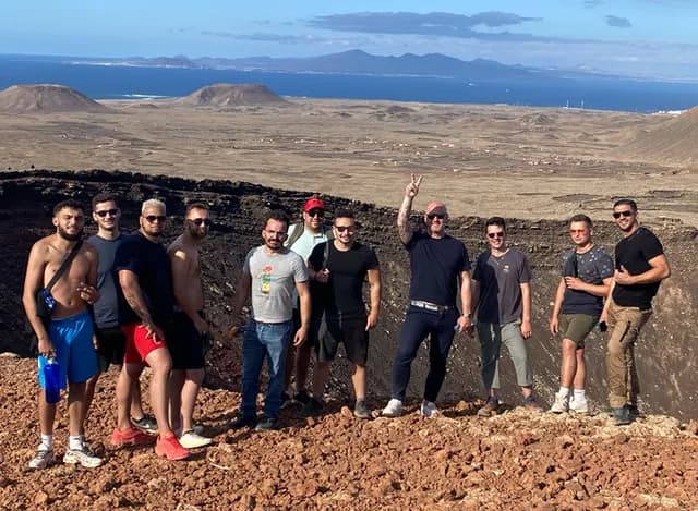 L'équipe Migen alignée au bord du cratère d'un volcan, l'océan au loin
