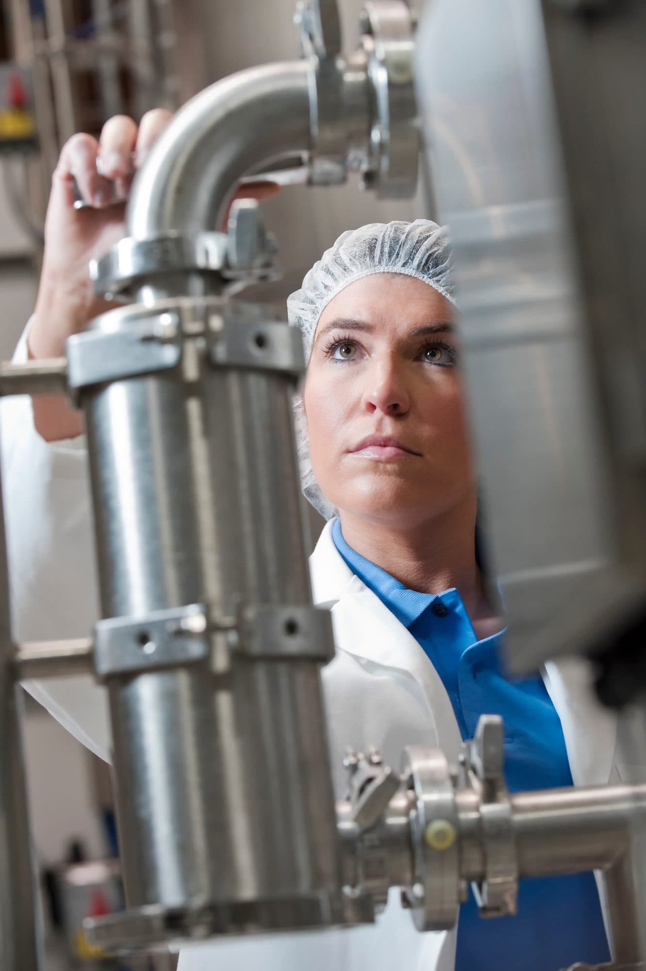 Technicienne en charlotte contrôlant une tuyauterie de process inox
