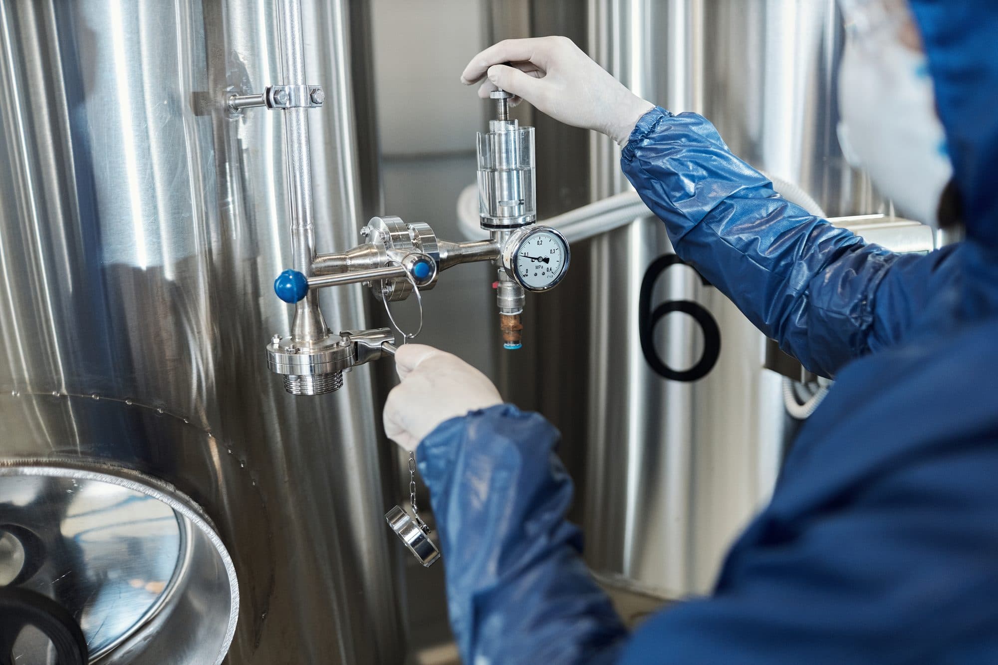 Mains gantées réglant un piquage avec manomètre sur une cuve inox