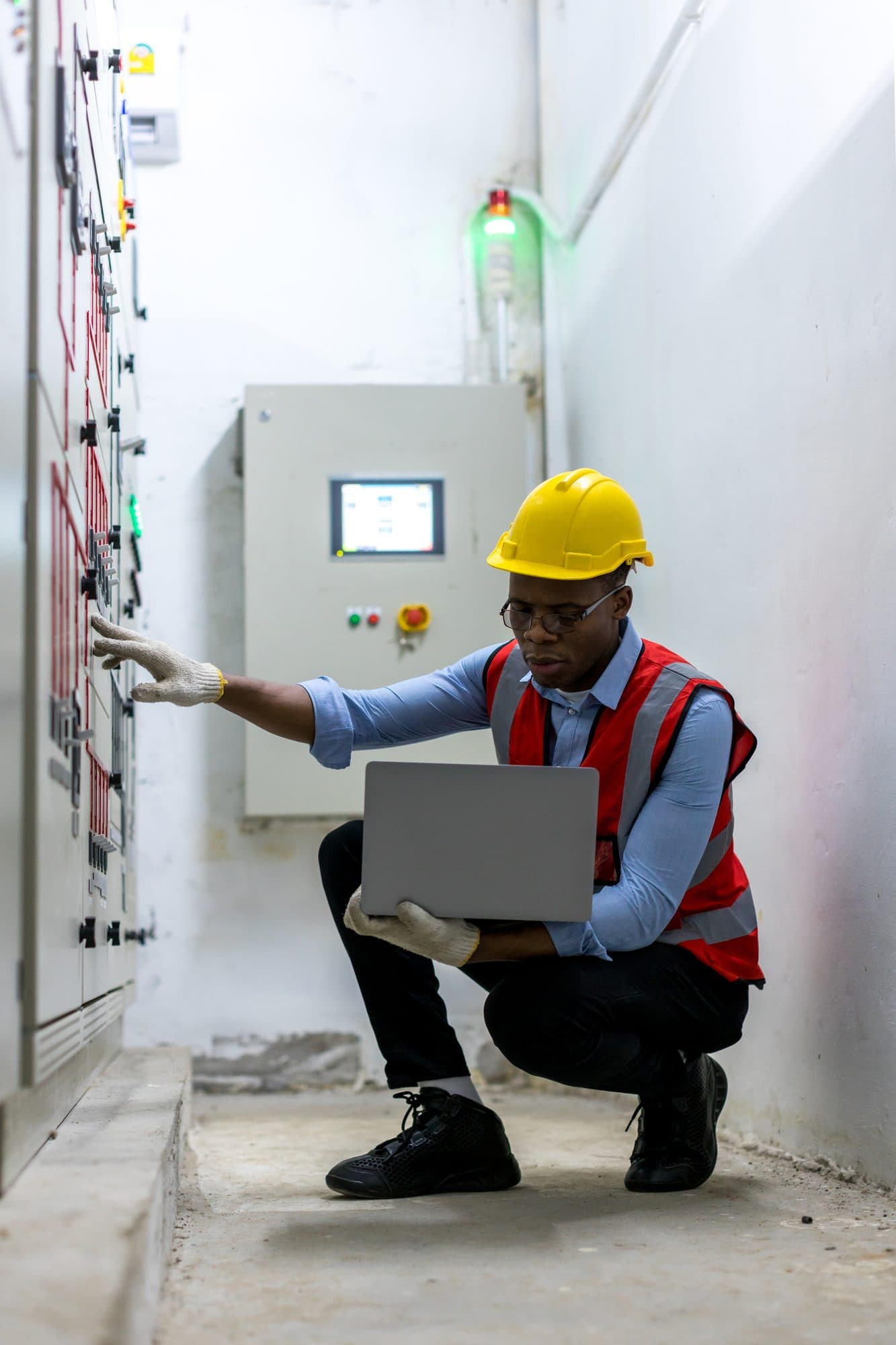 Technicien accroupi en local électrique, main sur le tableau