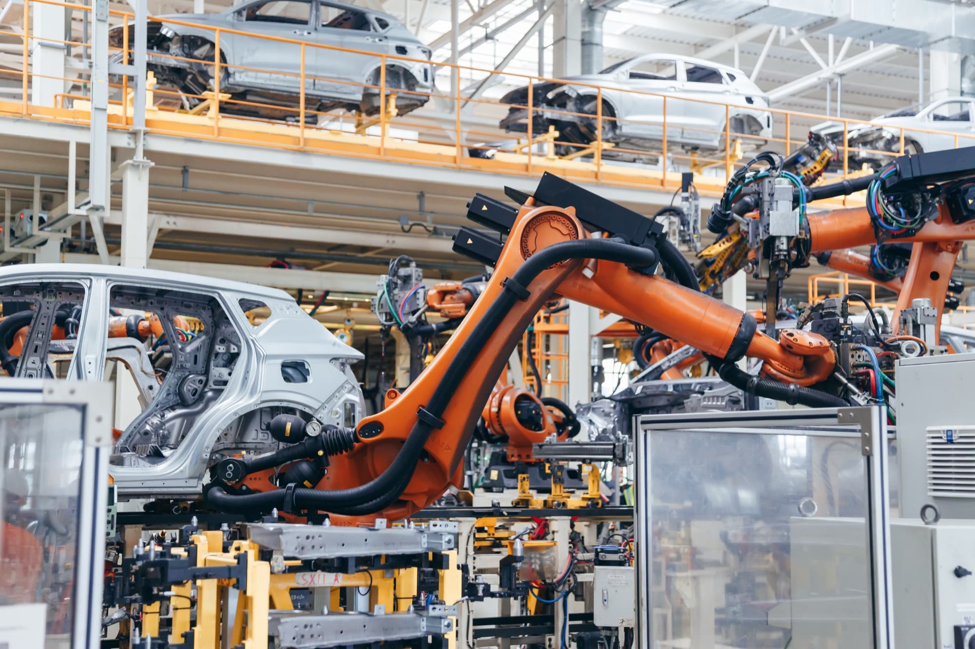 Bras robots orange alignés autour des caisses, sous le convoyeur aérien d'un atelier de carrosserie