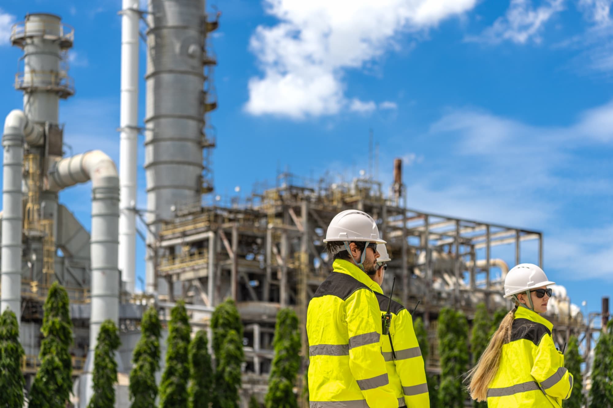 Deux intervenants en gilet jaune et casque longeant une unité pétrochimique