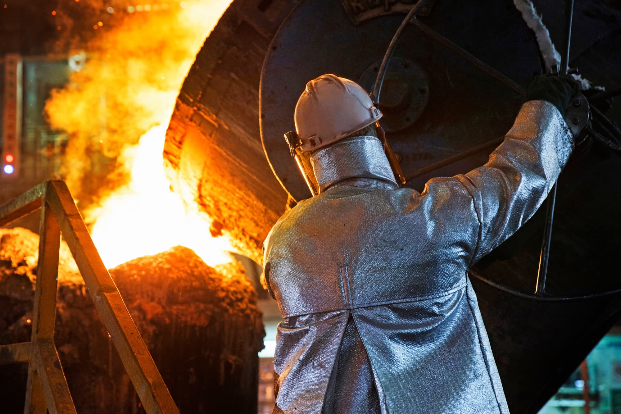Fondeur en veste aluminisée guidant à bout de bras une poche de coulée qui déverse l'acier liquide