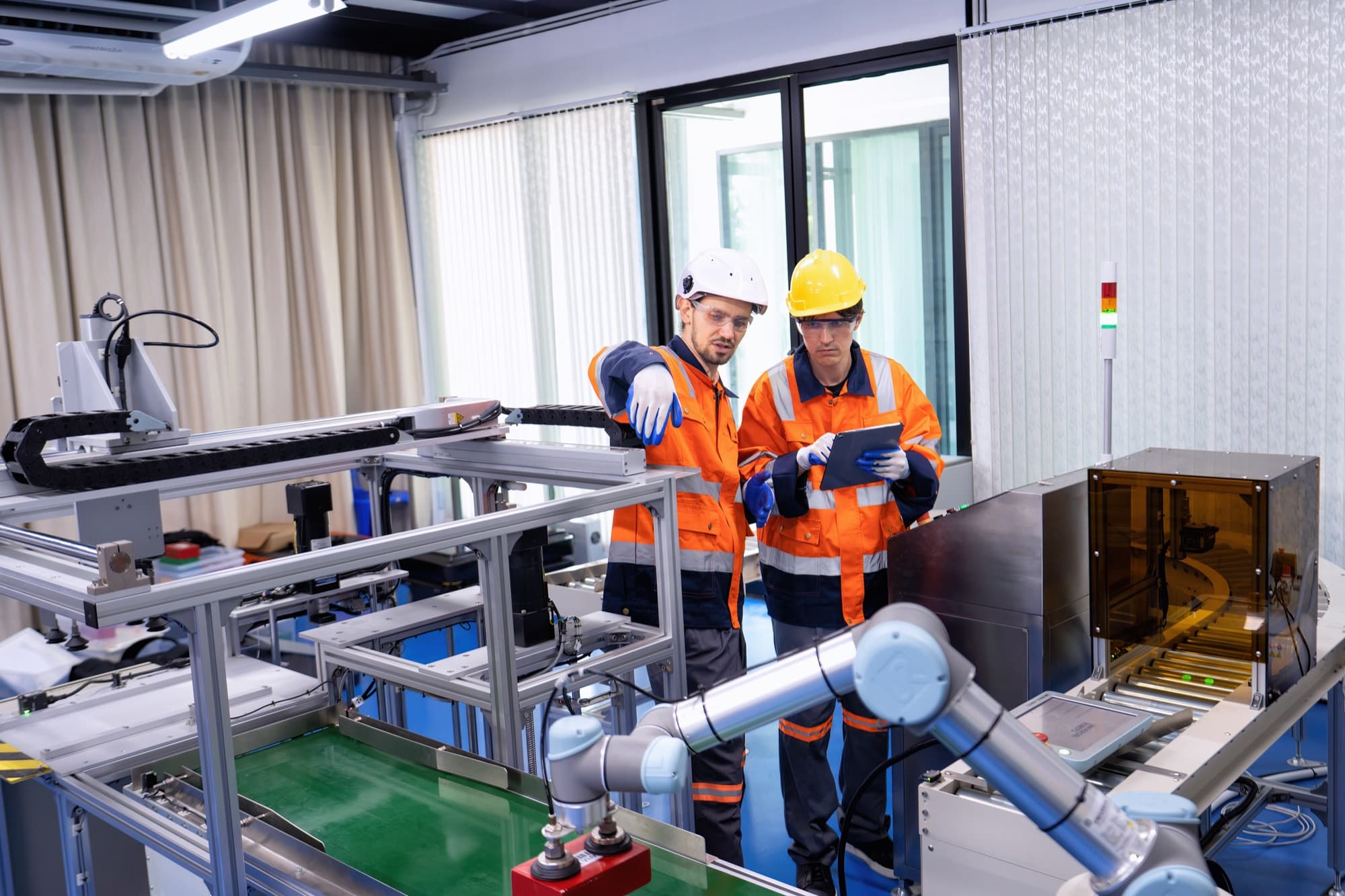 Deux techniciens en gilet orange réglant un cobot sur un banc de production automatisé, tablette en main