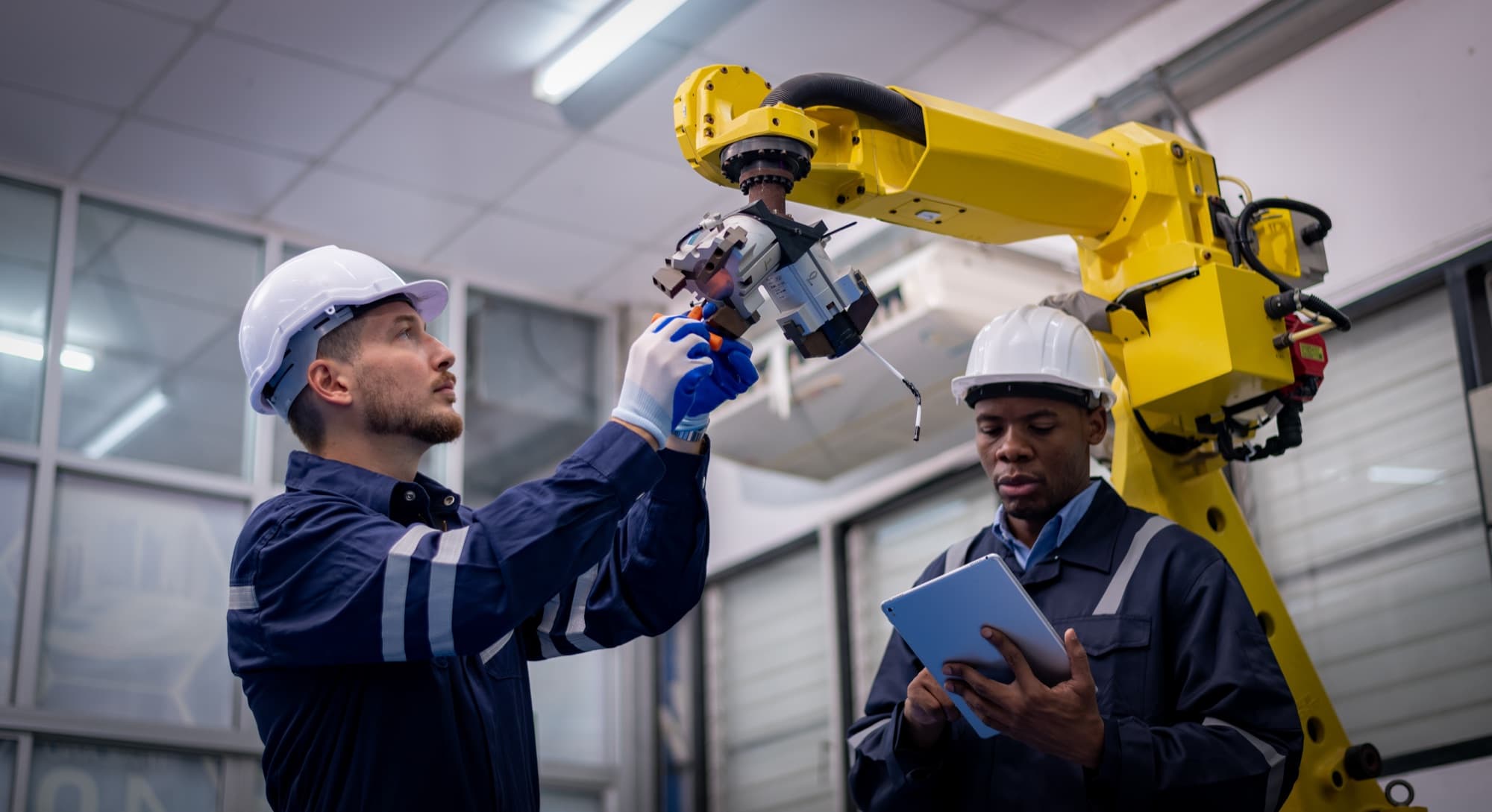 Deux techniciens casqués contrôlant le poignet et la pince d'un robot industriel jaune