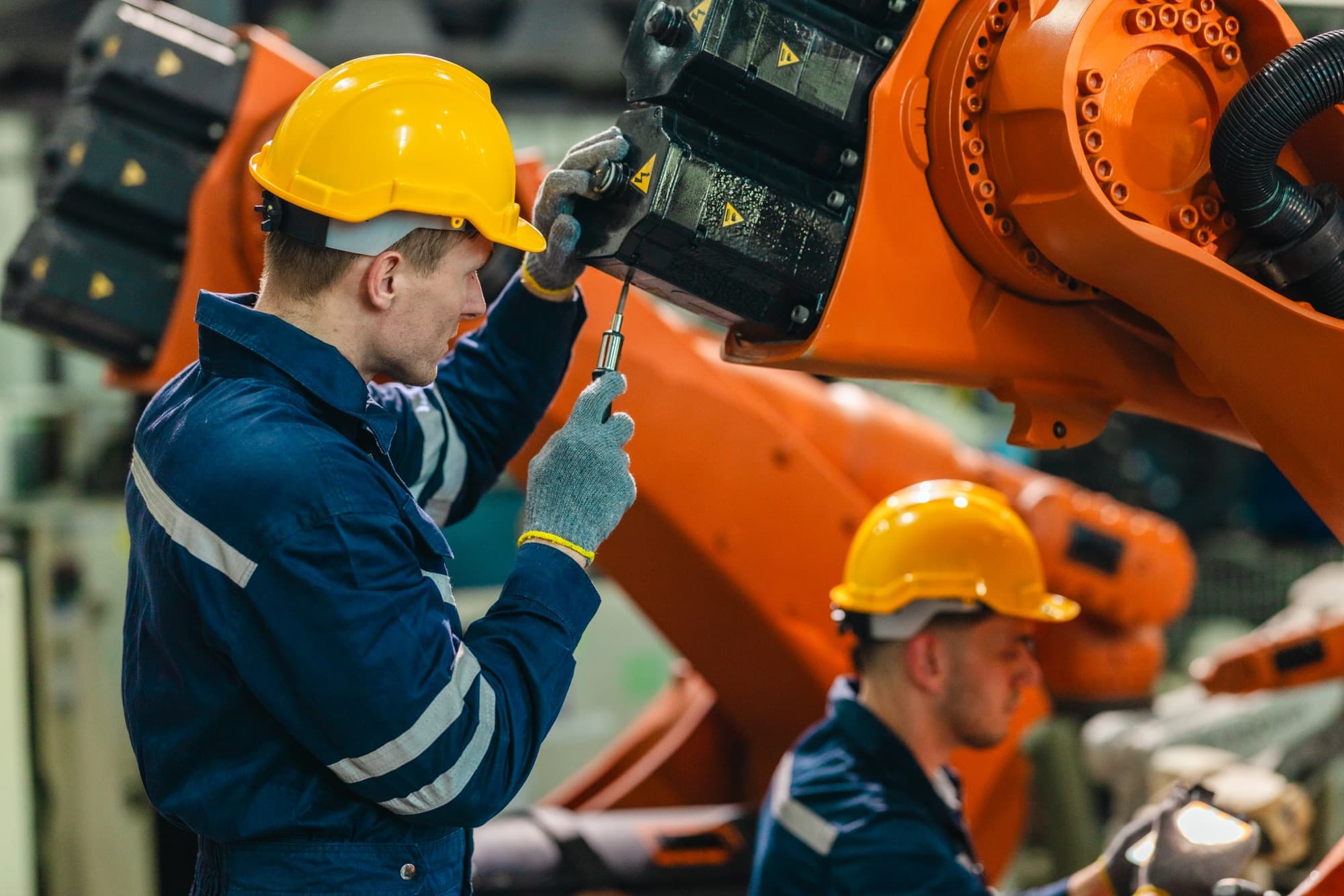 Technicien vissant une platine sur l'axe d'un robot orange, un second opérateur en arrière-plan