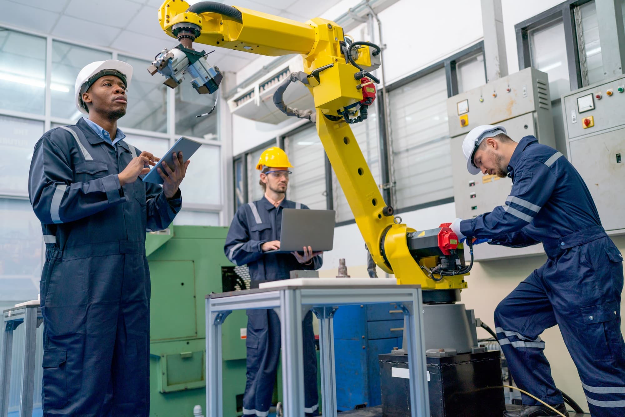 Trois techniciens mettant au point un robot jaune, tablette et ordinateur portable en main