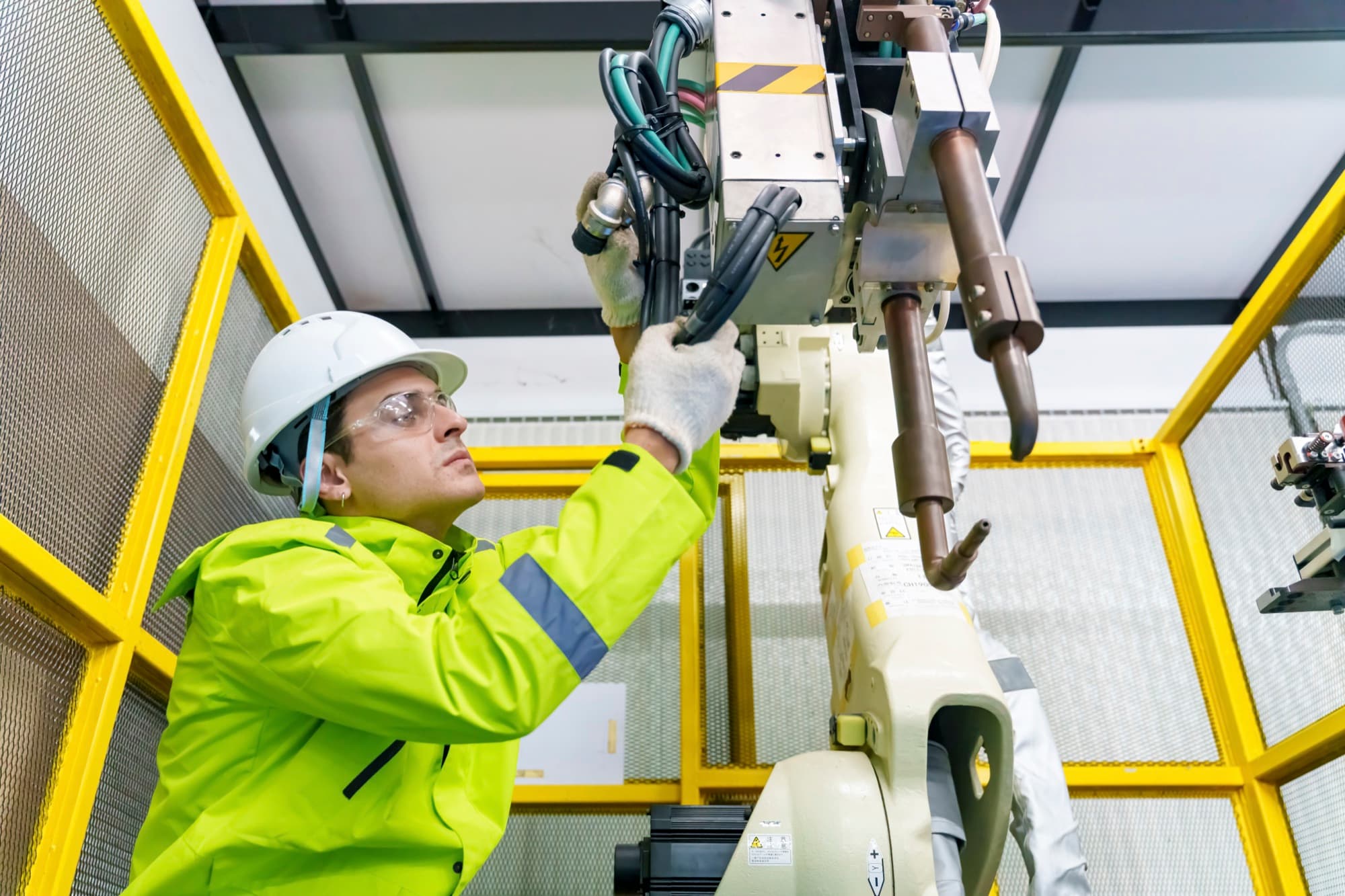 Technicien en gilet fluo intervenant bras levés sur un robot à l'intérieur de sa cage de sécurité