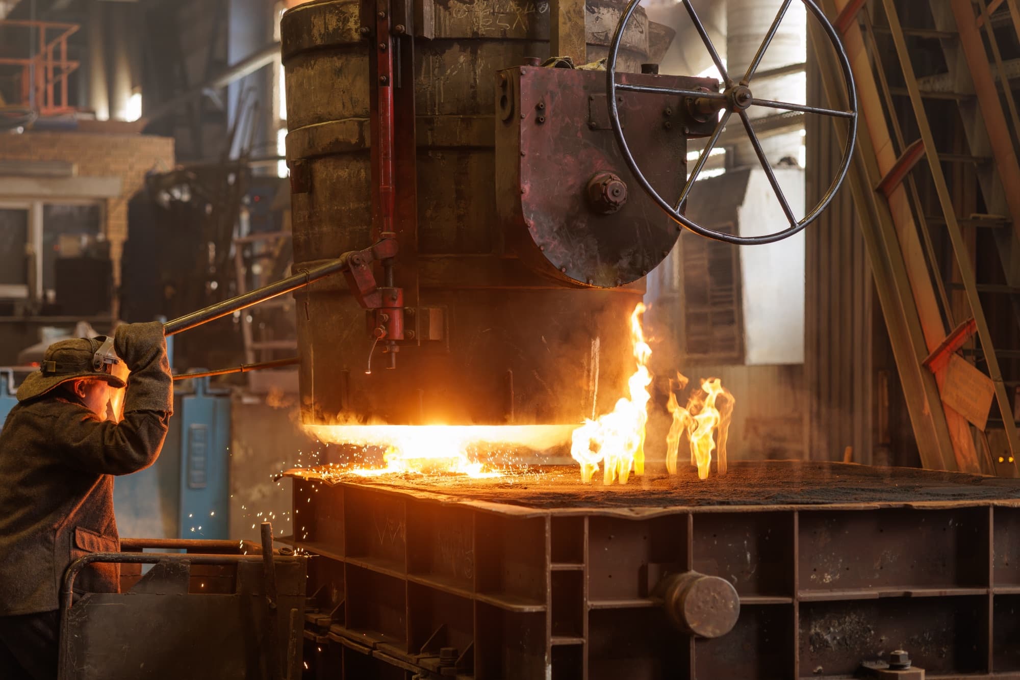 Ouvrier guidant à la perche une pièce incandescente sous une presse à volant dans une forge
