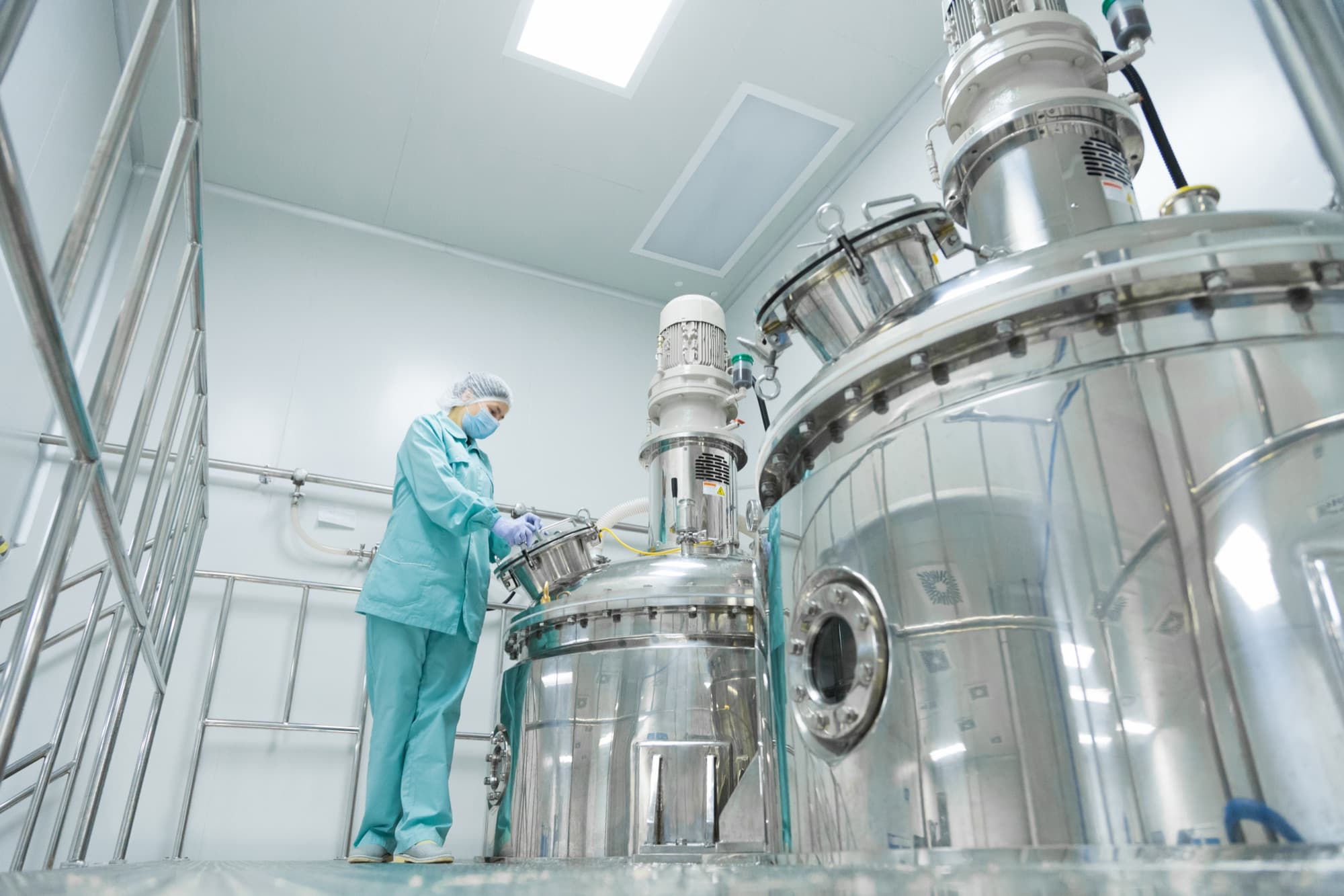 Technicienne en tenue stérile refermant la trappe d'une cuve inox de mélange en salle blanche