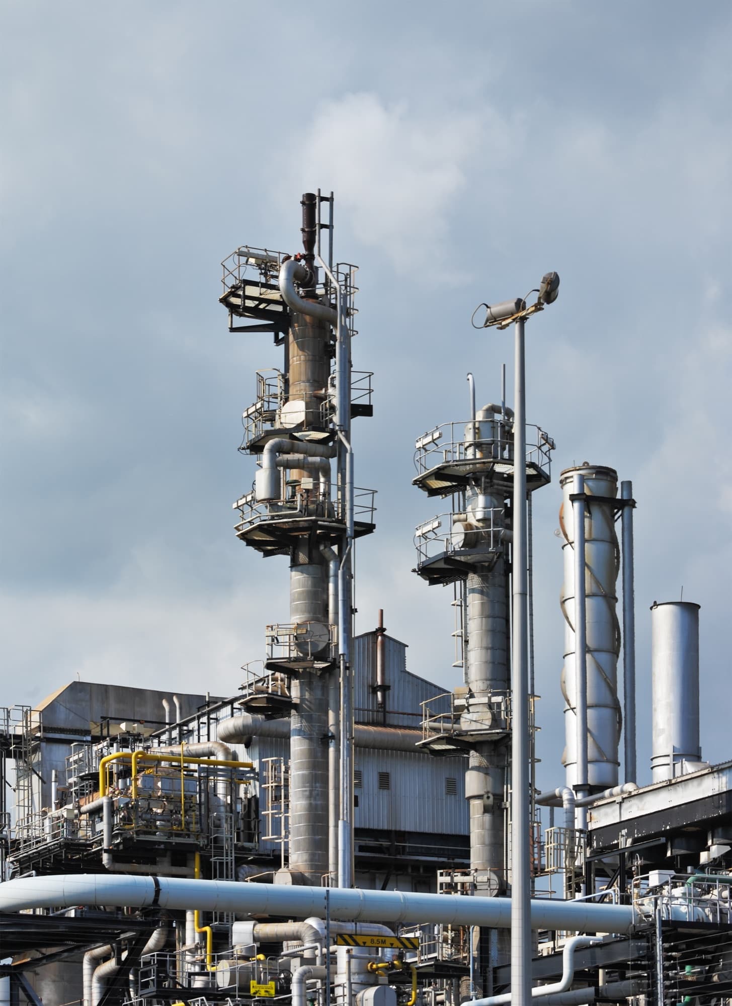 Deux colonnes de distillation et leurs passerelles d'accès dans une raffinerie, ciel couvert