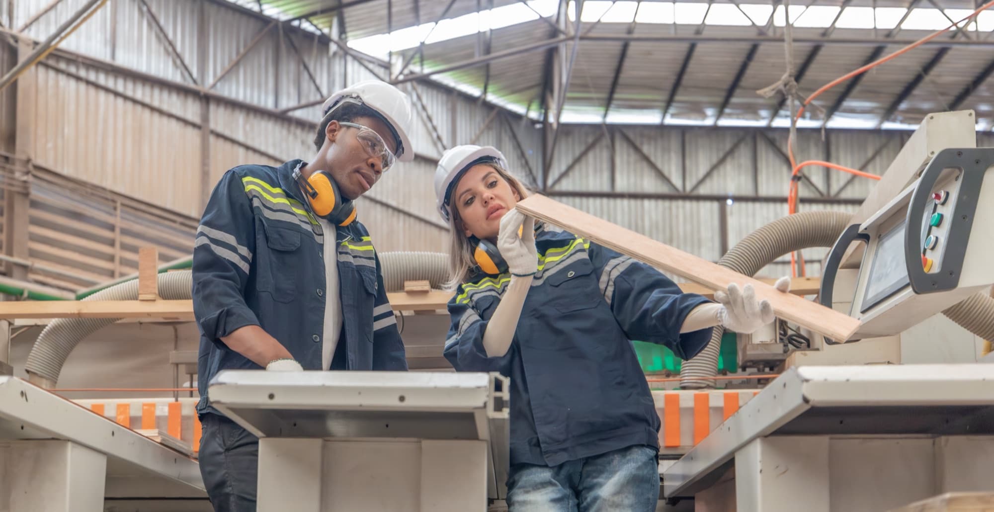 Deux opérateurs casqués contrôlant une planche à la sortie d'une machine à bois à commande numérique