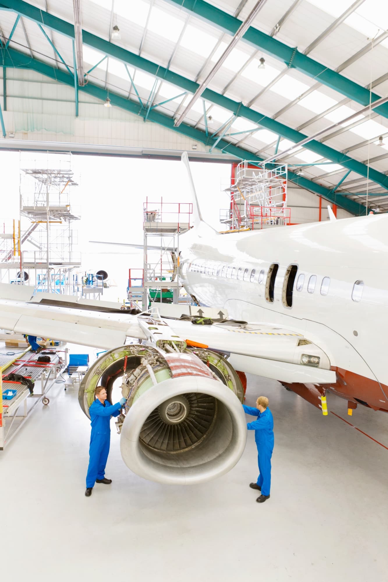 Vue verticale d'un hangar de maintenance, deux mécaniciens de part et d'autre d'un réacteur capot ouvert