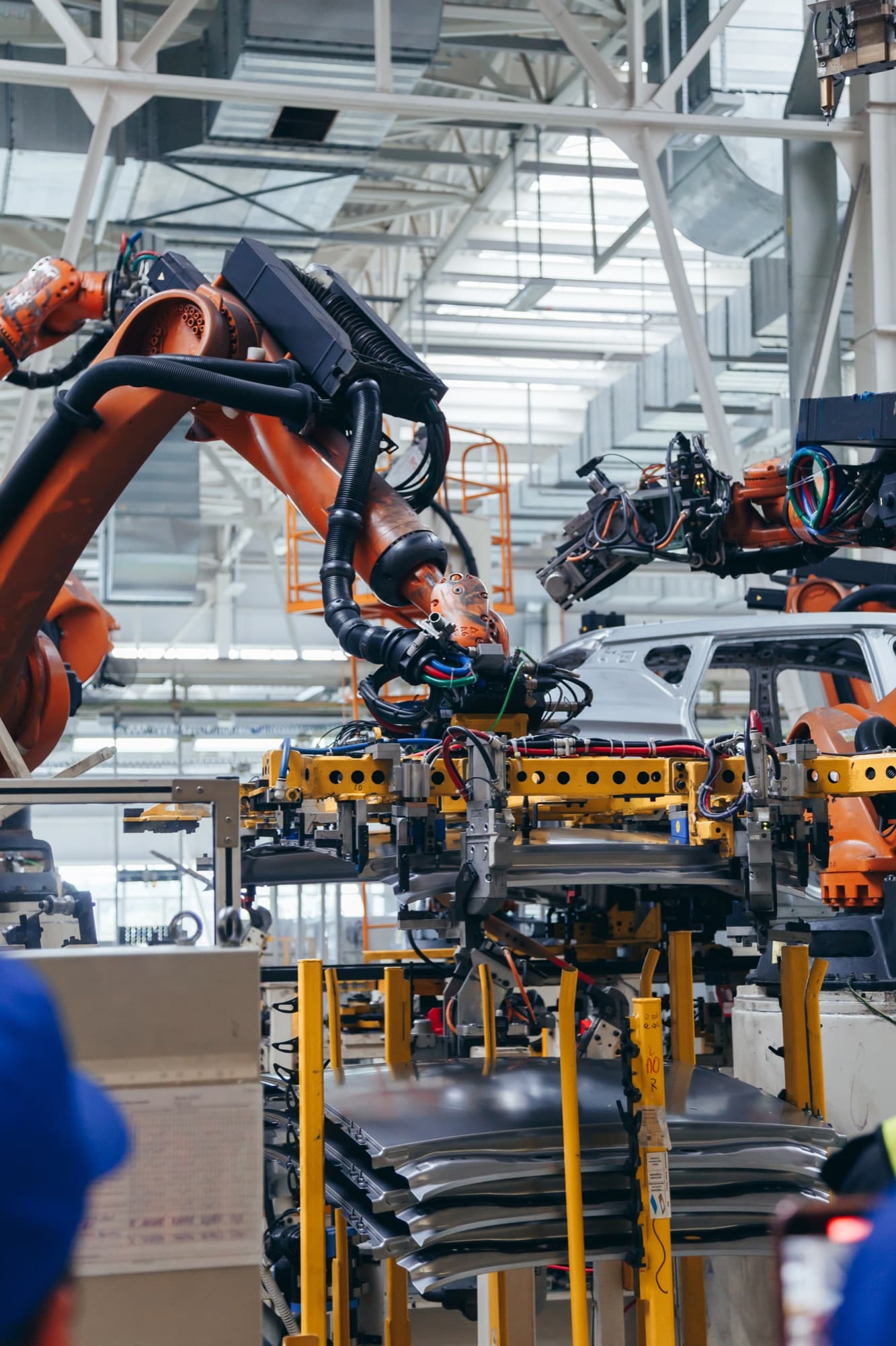 Bras robotisés orange manipulant des pièces de carrosserie sur une ligne d'assemblage automobile