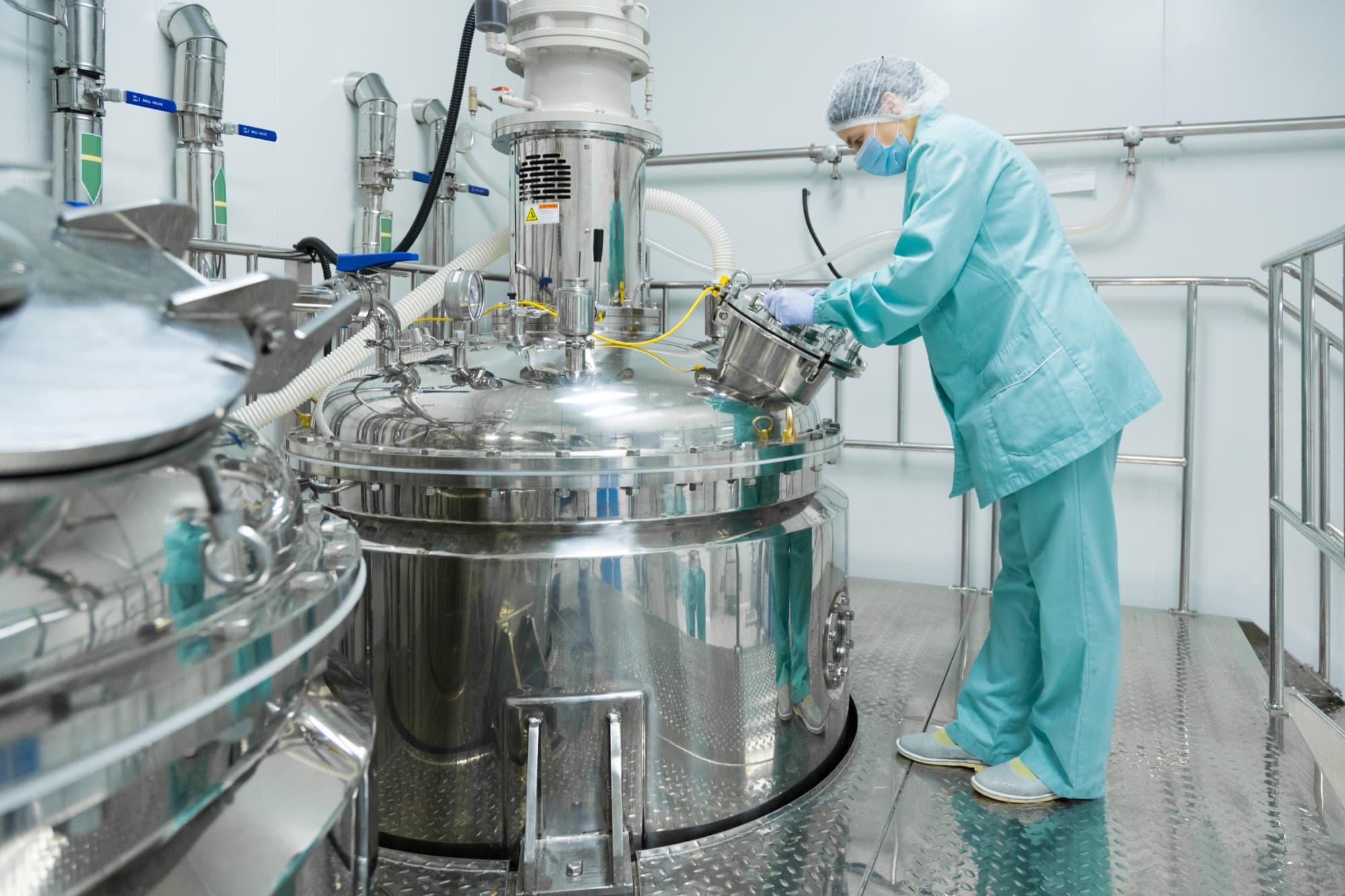 Opératrice en tenue stérile intervenant sur la trappe d'un réacteur inox de production en salle blanche