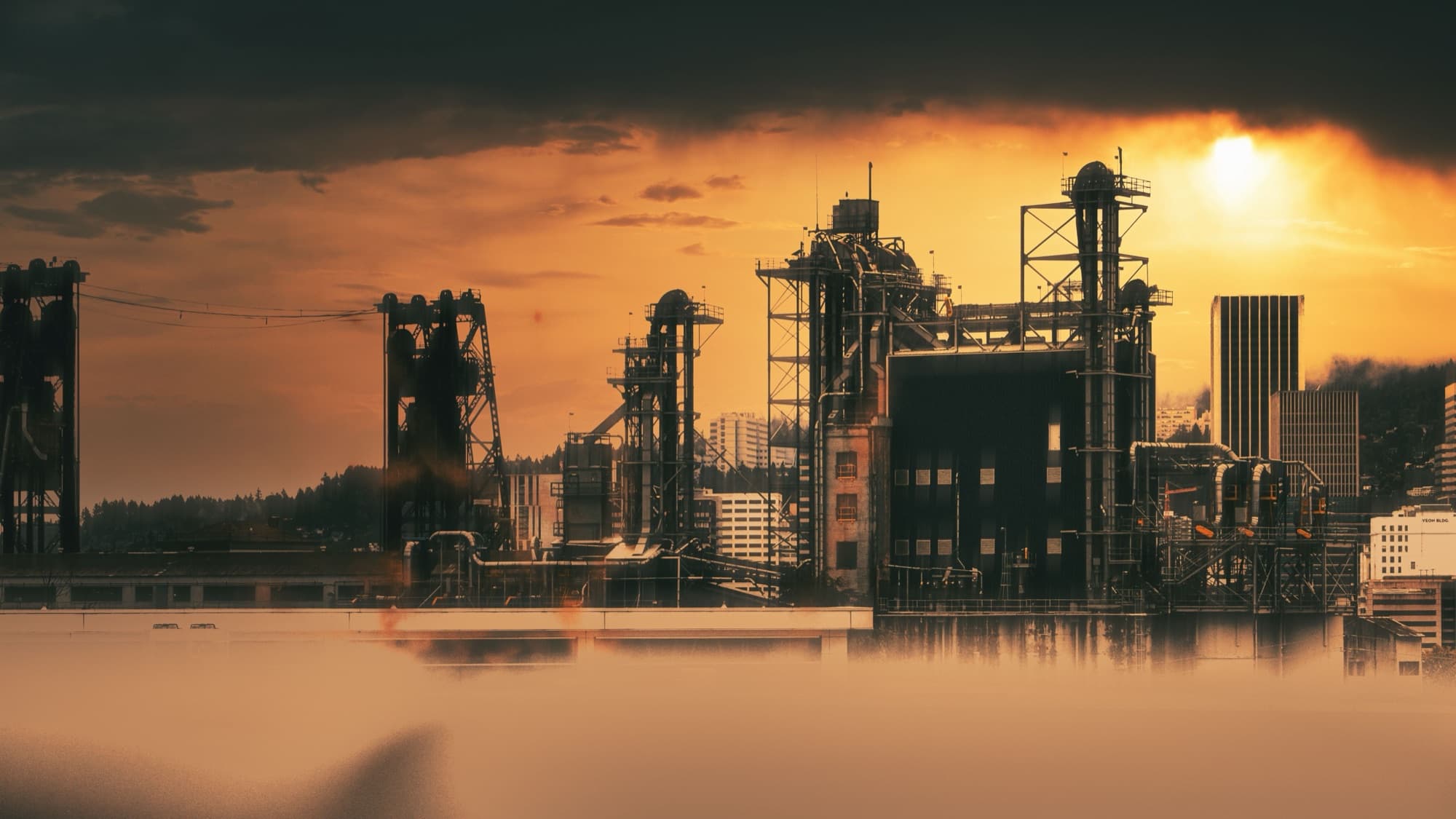Silhouettes de silos et d'élévateurs industriels au coucher du soleil, ville en arrière-plan