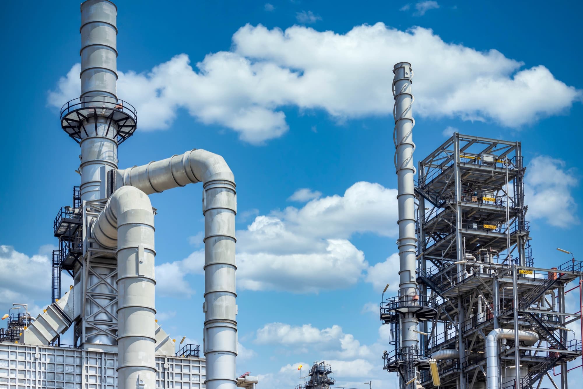 Colonnes, gaines et passerelles d'une unité pétrochimique se détachant sur un ciel bleu nuageux