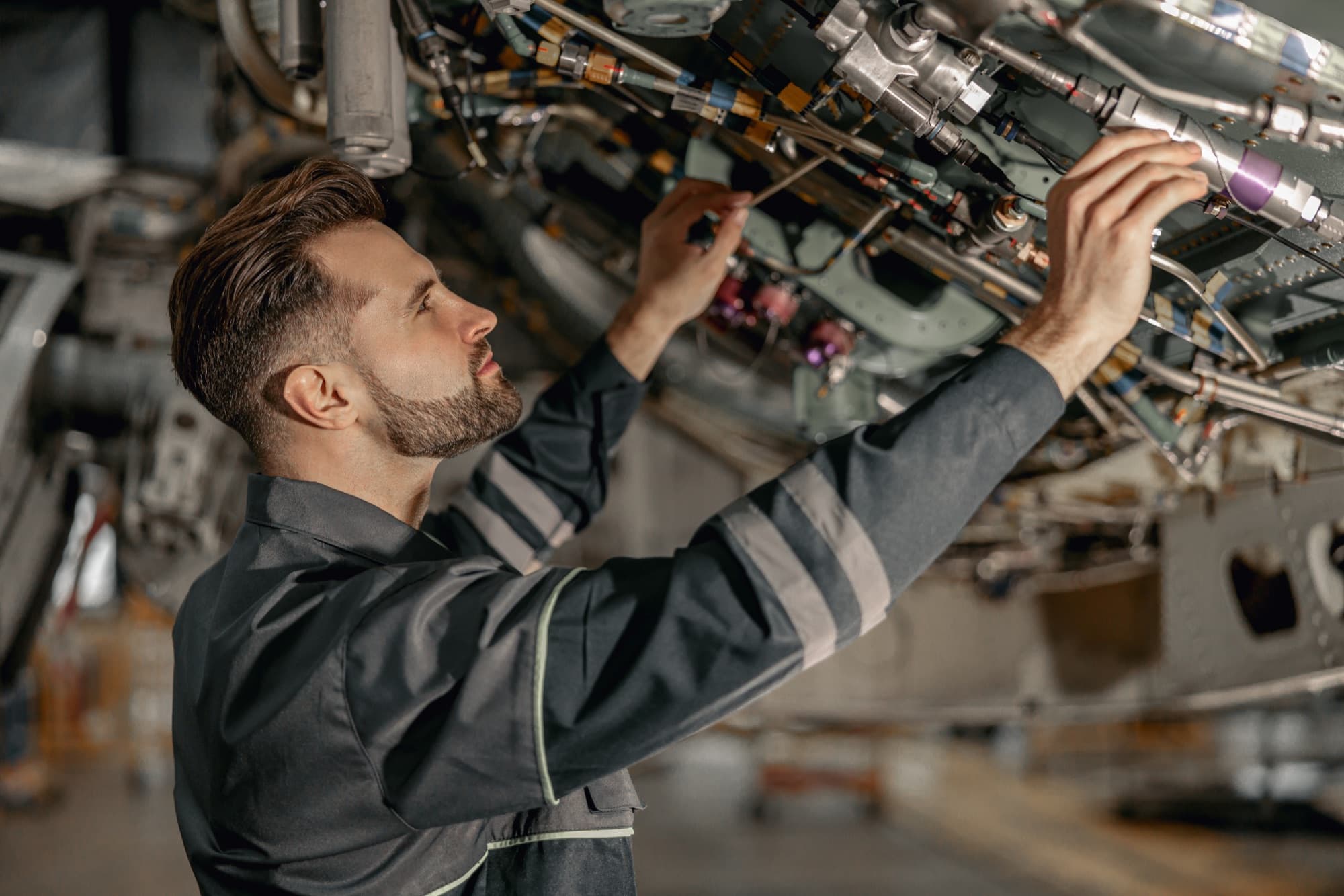 Technicien réglant les circuits et raccords sous la cellule d'un aéronef en hangar