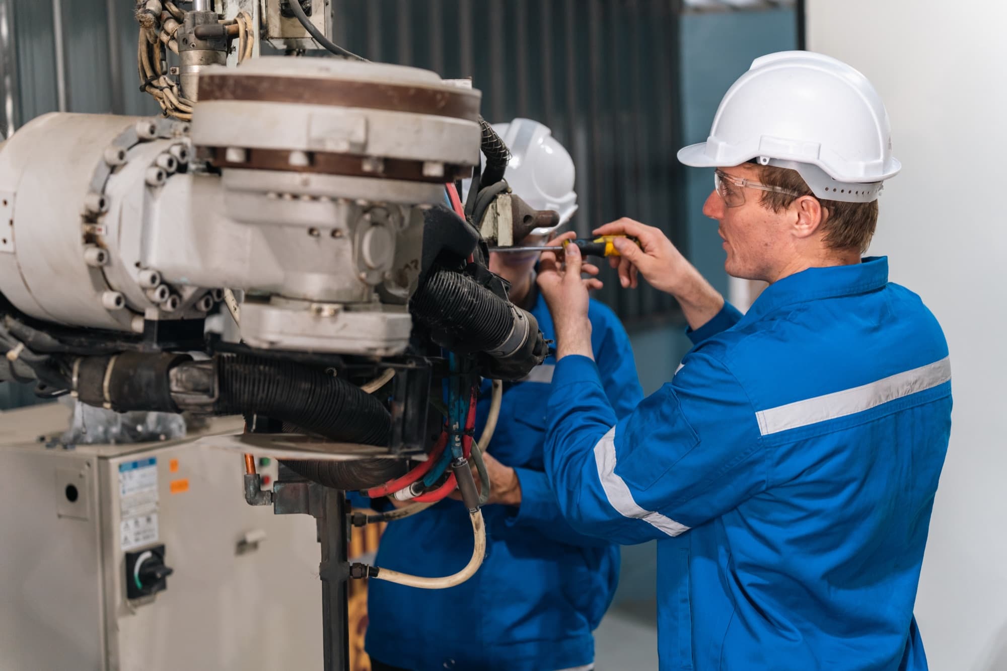 Deux techniciens en bleu de travail intervenant à la clé sur la tête articulée d'une grosse machine en atelier