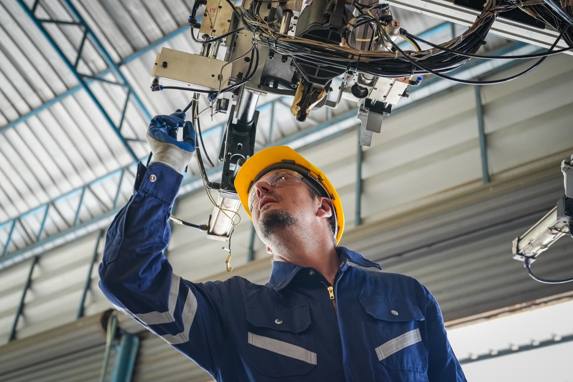 Technicien en casque jaune contrôlant un outillage suspendu à la charpente d'une halle de production