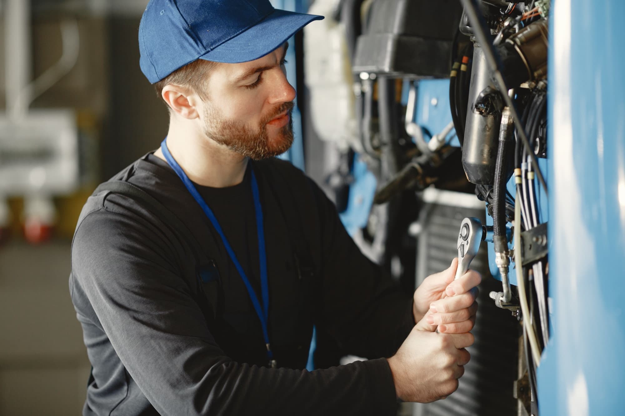Technicien à la clé à cliquet sur le flanc d'une machine bleue garnie de flexibles, dans un atelier