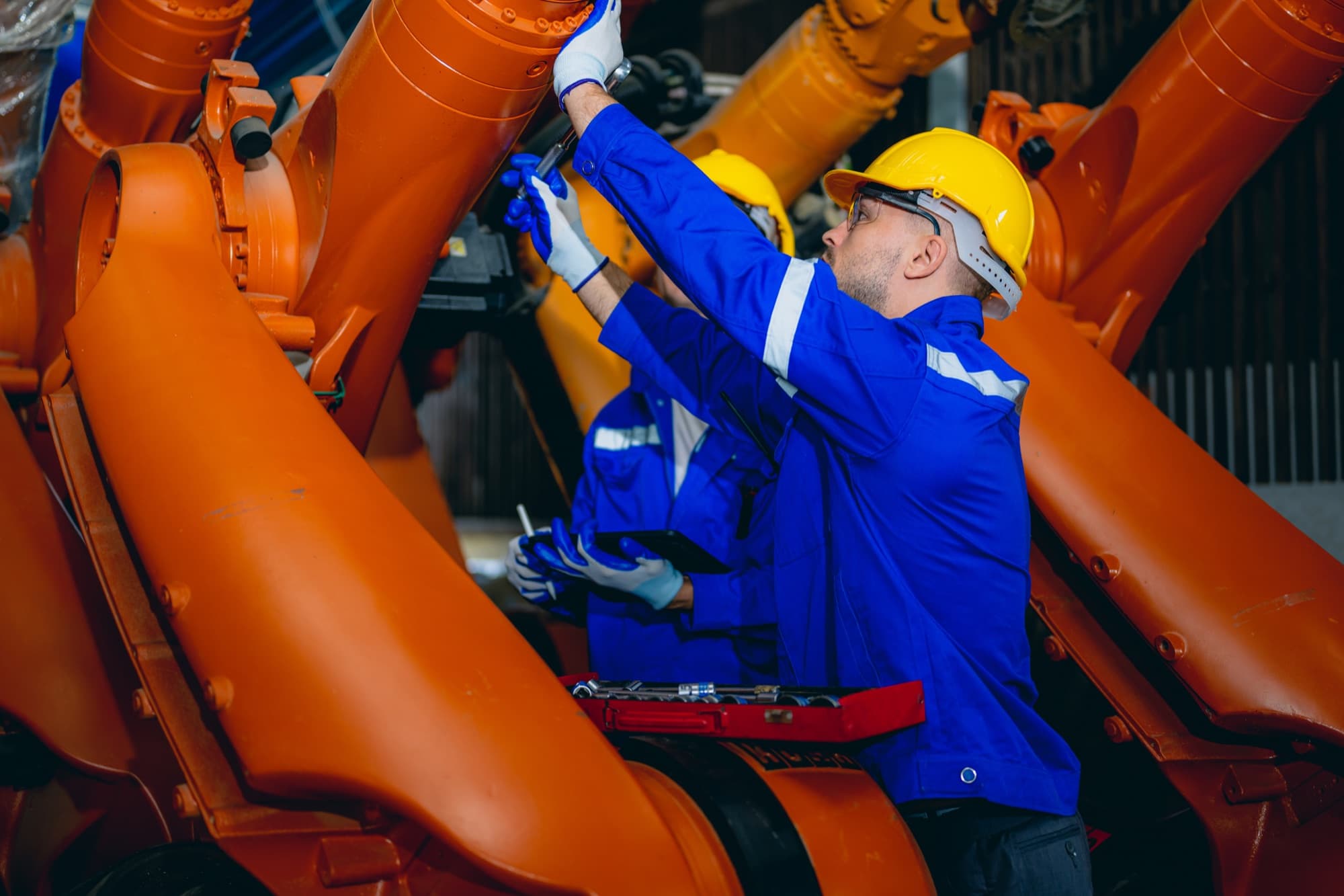 Deux techniciens intervenant à la clé sur des bras robotisés orange alignés dans un atelier