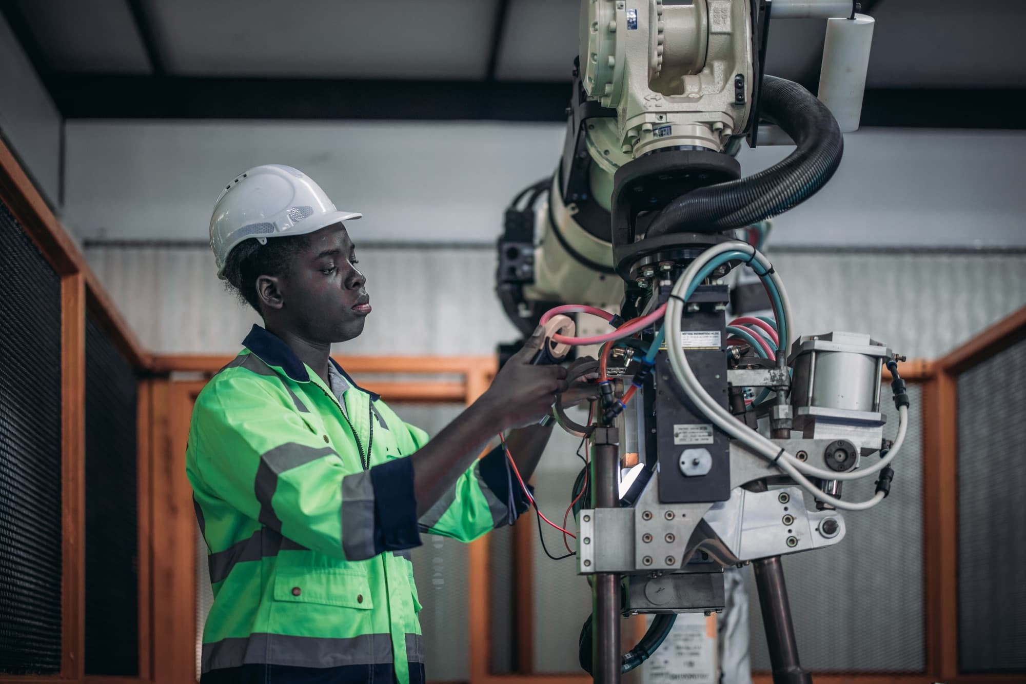 Technicien en gilet vert raccordant les câbles de l'outil terminal d'un robot industriel