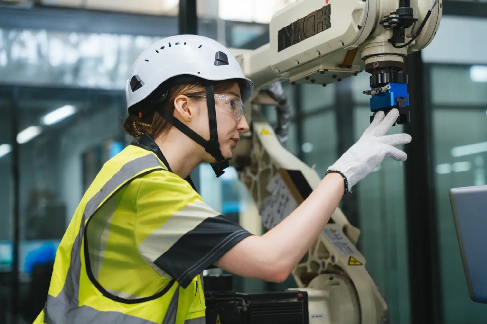 Technicienne en casque et gilet haute visibilité ajustant la pince en bout de bras d'un robot industriel