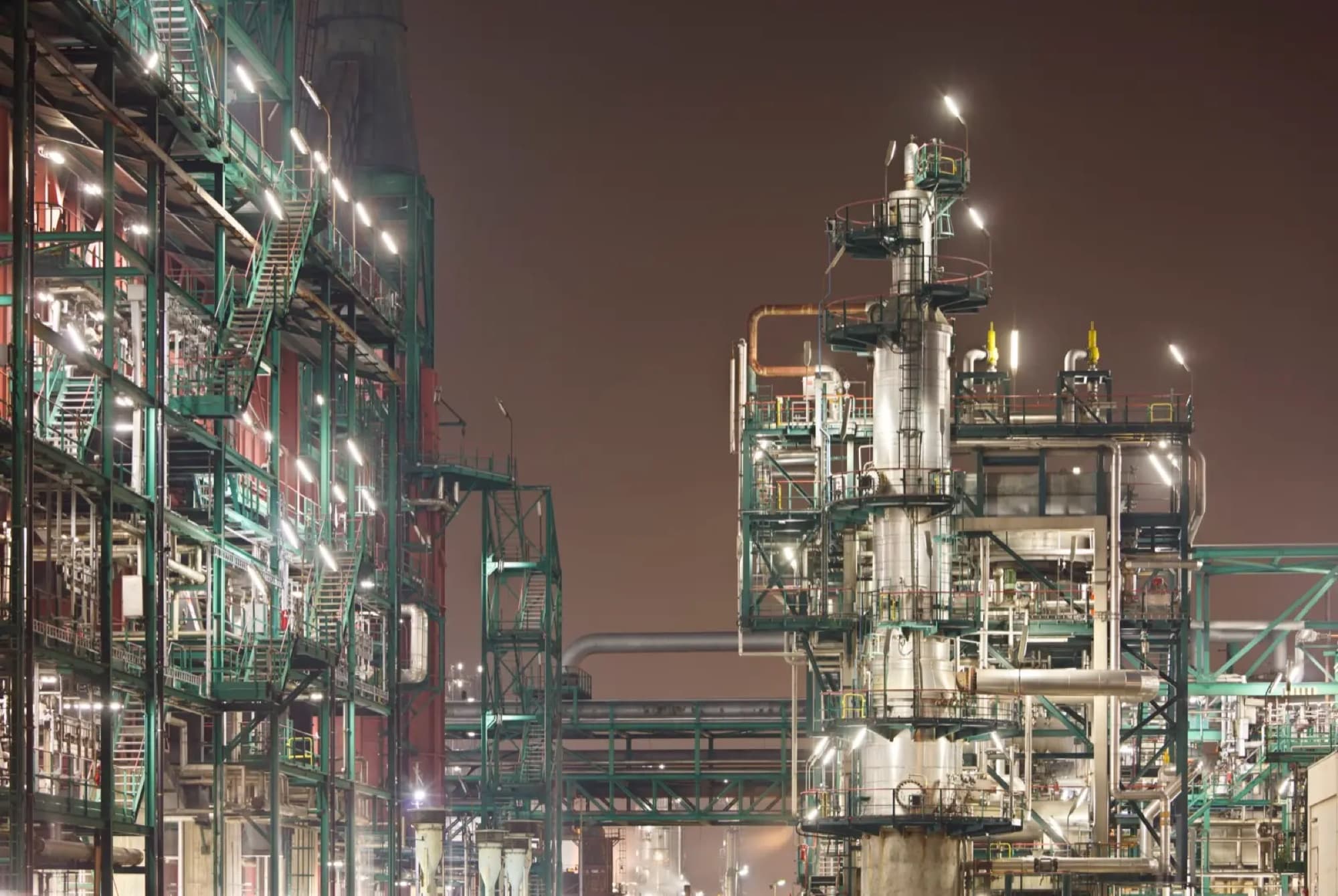 Colonnes de distillation et racks de tuyauterie d'une raffinerie éclairés en pleine nuit