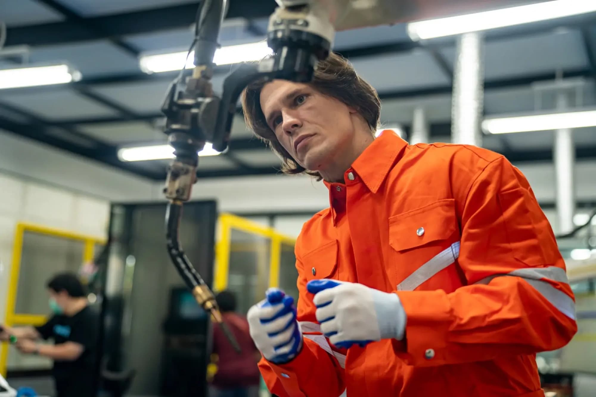 Technicien en combinaison orange réglant la torche de soudage montée en bout d'un bras robotisé