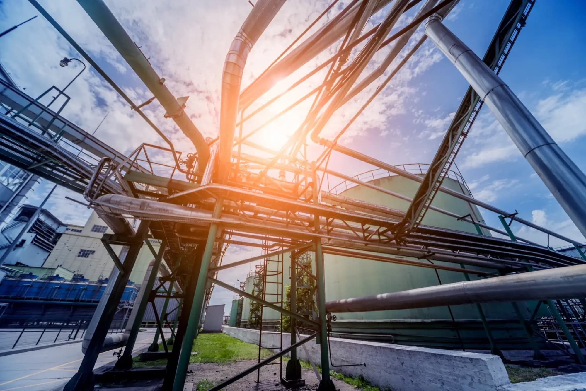 Rack de tuyauterie et bacs de stockage d'un site pétrochimique vus en contre-plongée à contre-jour