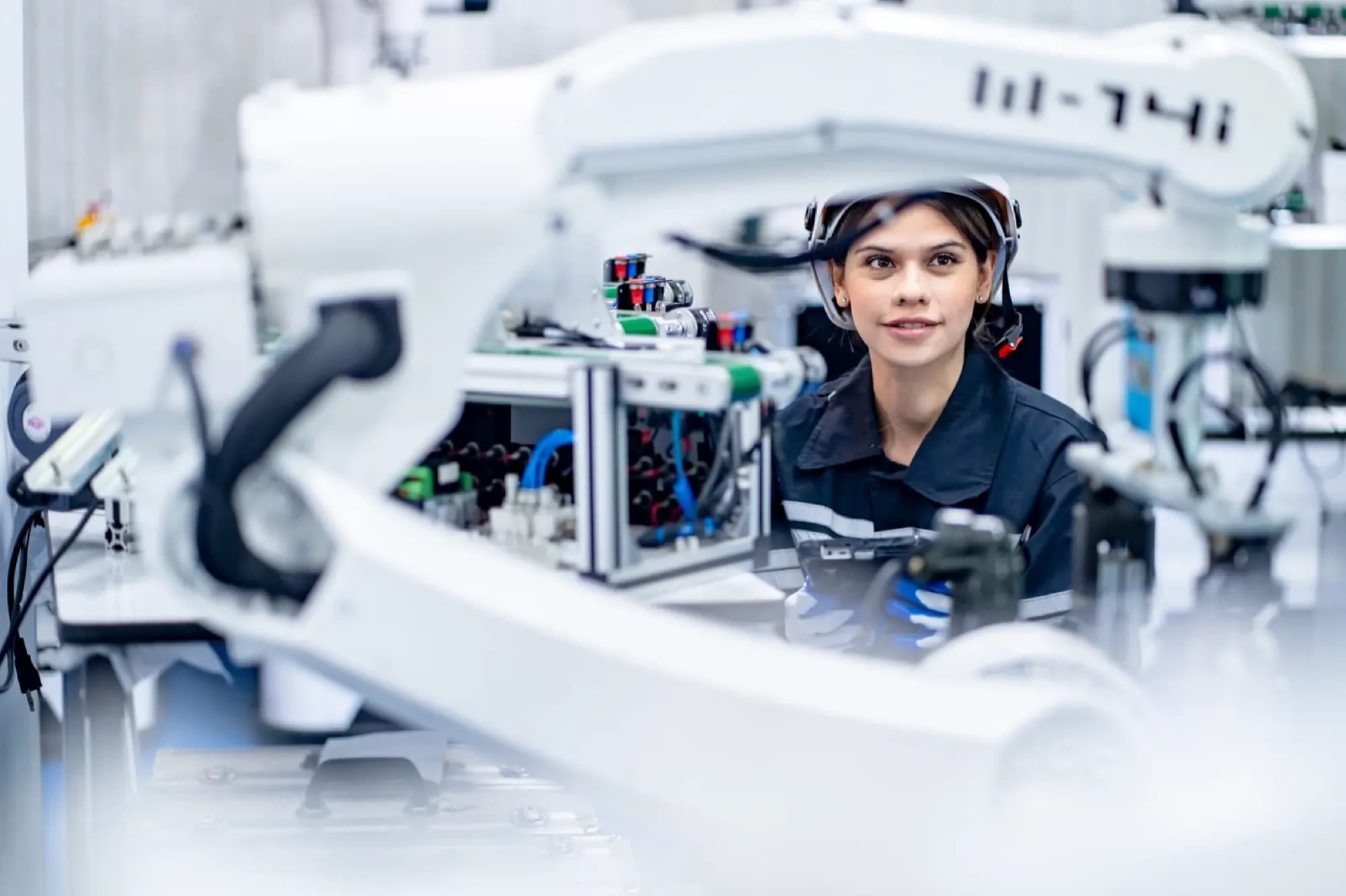 Technicienne en visière de protection derrière un bras robotique blanc et un banc d'essai câblé