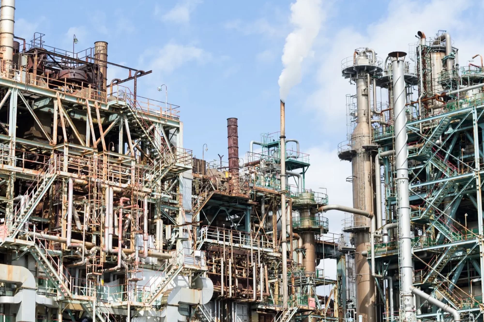 Complexe pétrochimique vieillissant, colonnes, charpentes et tuyauterie rouillées sous ciel bleu