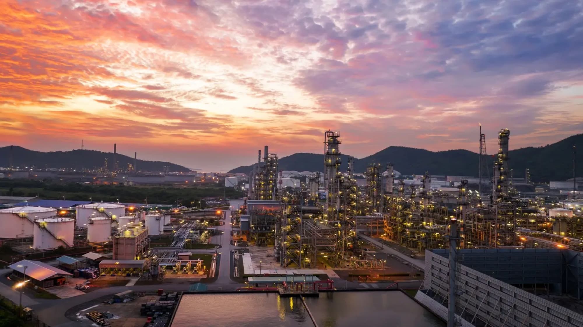 Vue aérienne d'une raffinerie éclairée au coucher du soleil, bacs de stockage et torchère allumée
