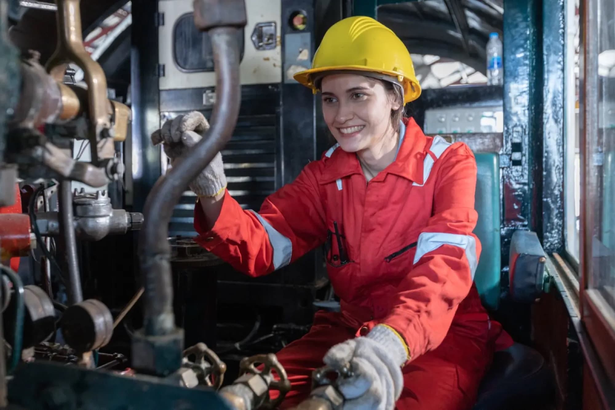 Technicienne en combinaison rouge actionnant une manette de commande dans la cabine d'une locomotive