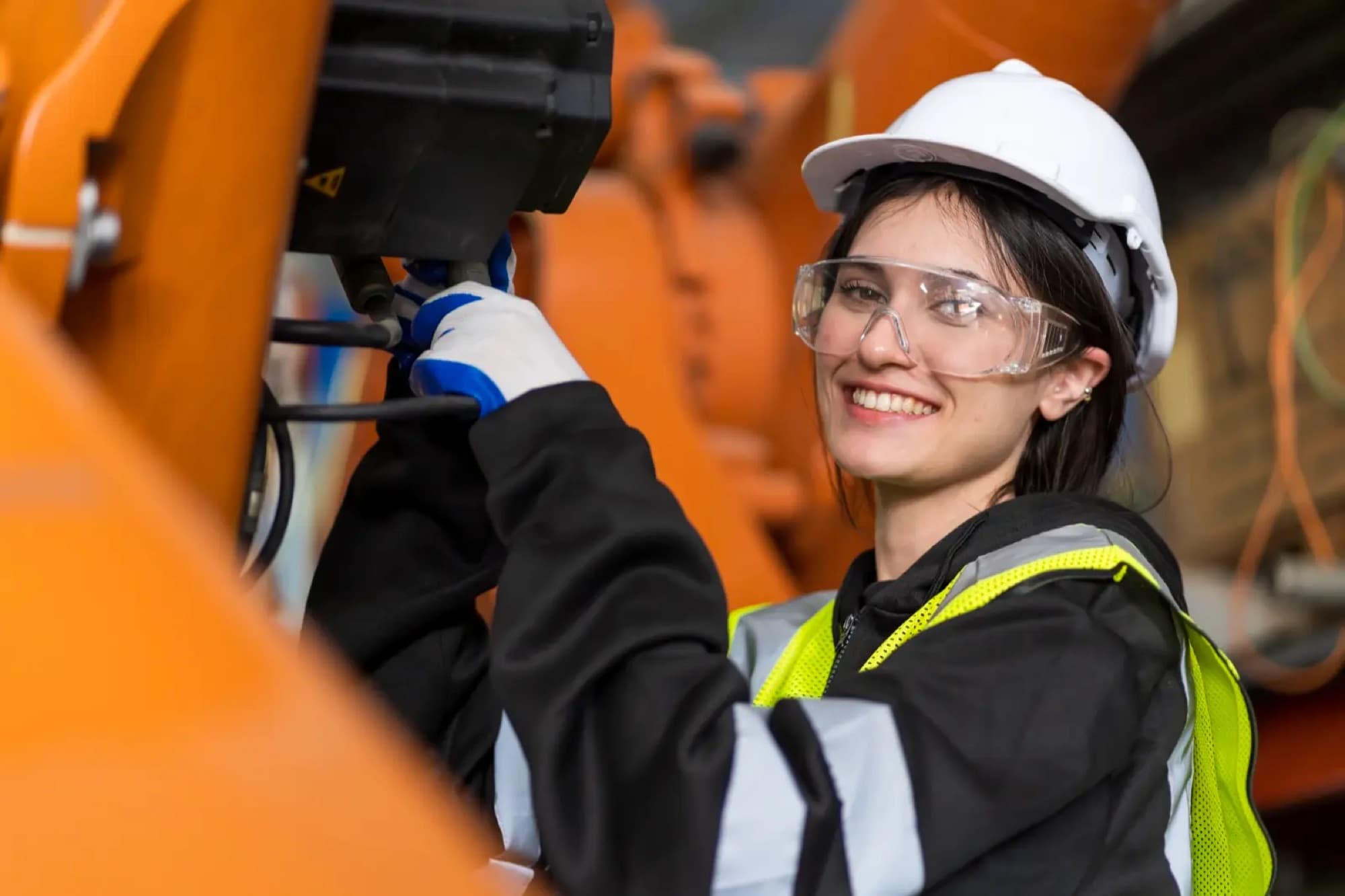 Technicienne la main sur l'outil en bout de bras d'un robot industriel orange