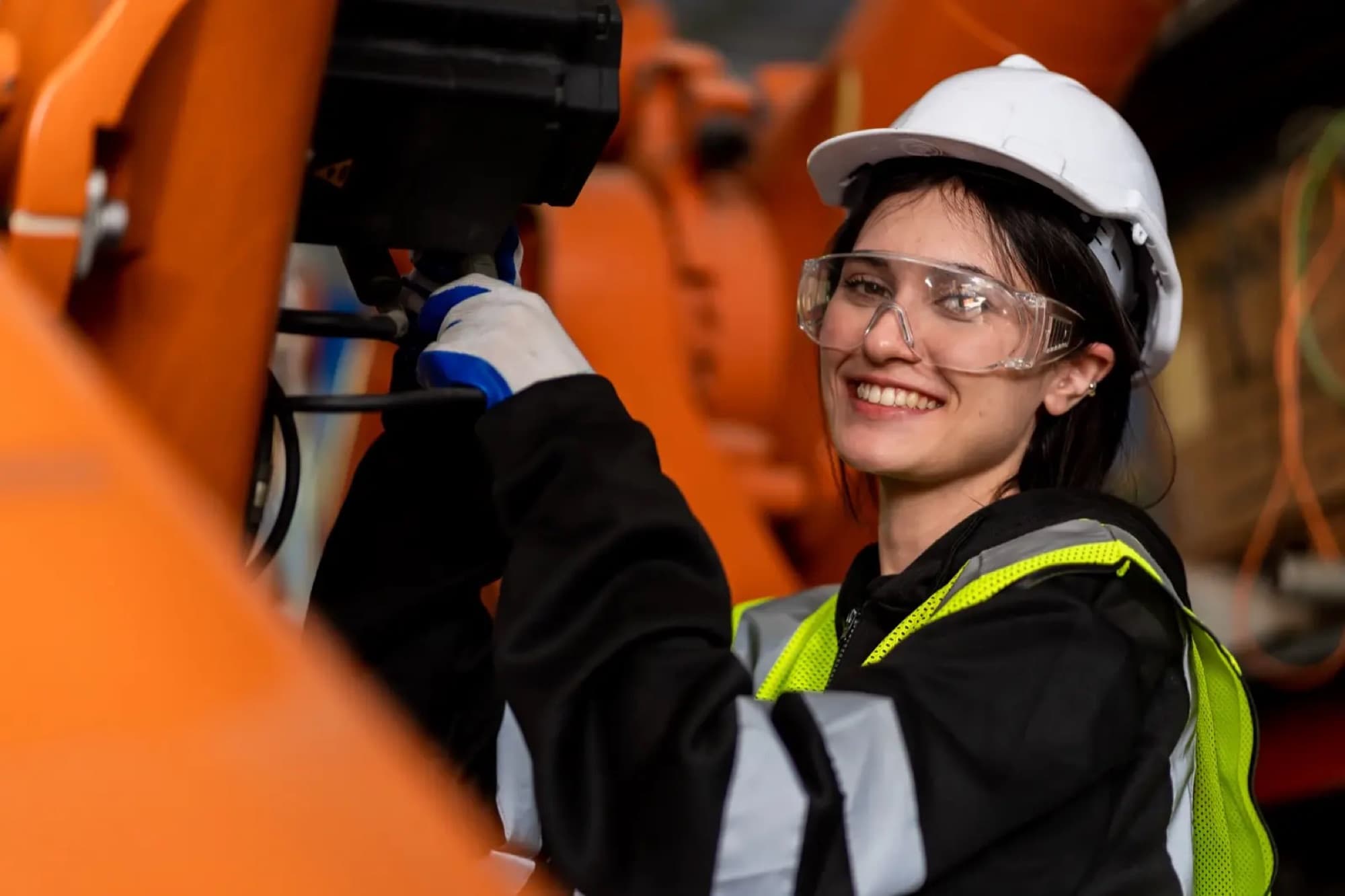 Technicienne gantée intervenant sur l'axe d'un bras robotisé orange en atelier