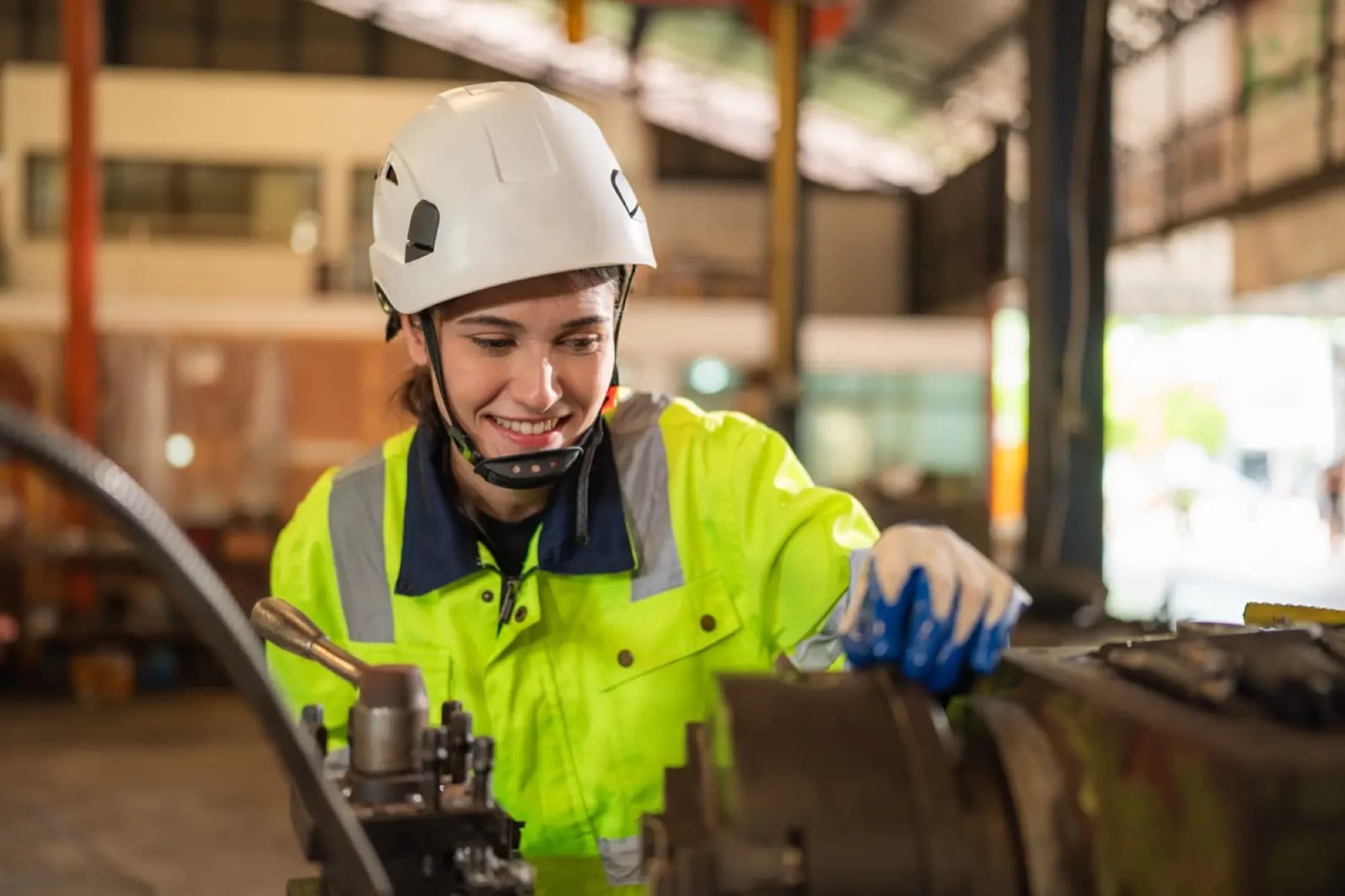 Technicienne en veste haute visibilité réglant la commande d'une machine-outil sous la halle d'atelier