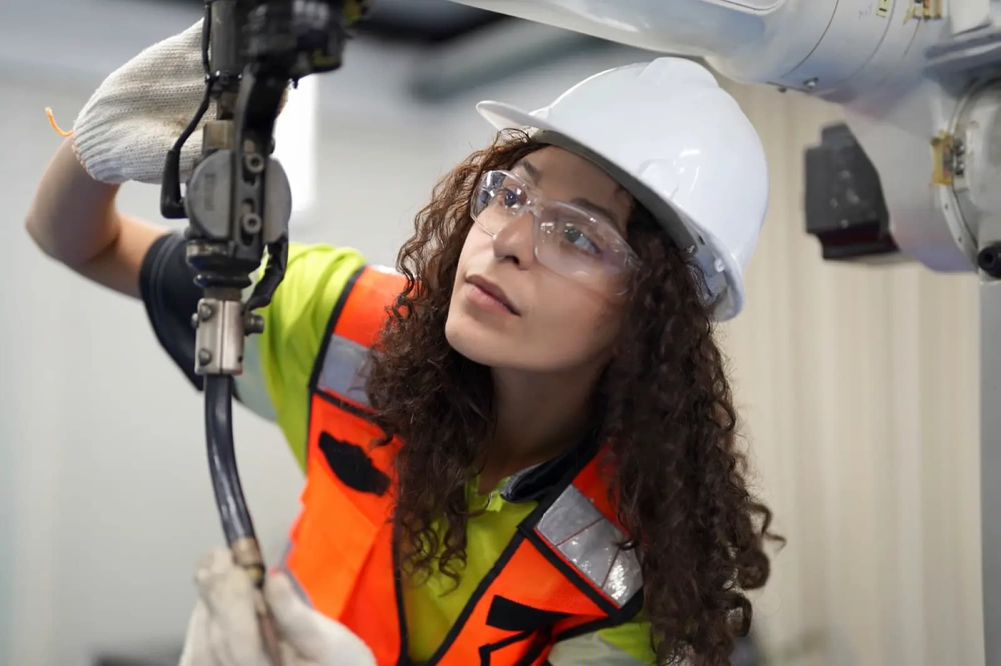 Technicienne en gilet orange contrôlant l'outil monté en bout d'un bras robotisé