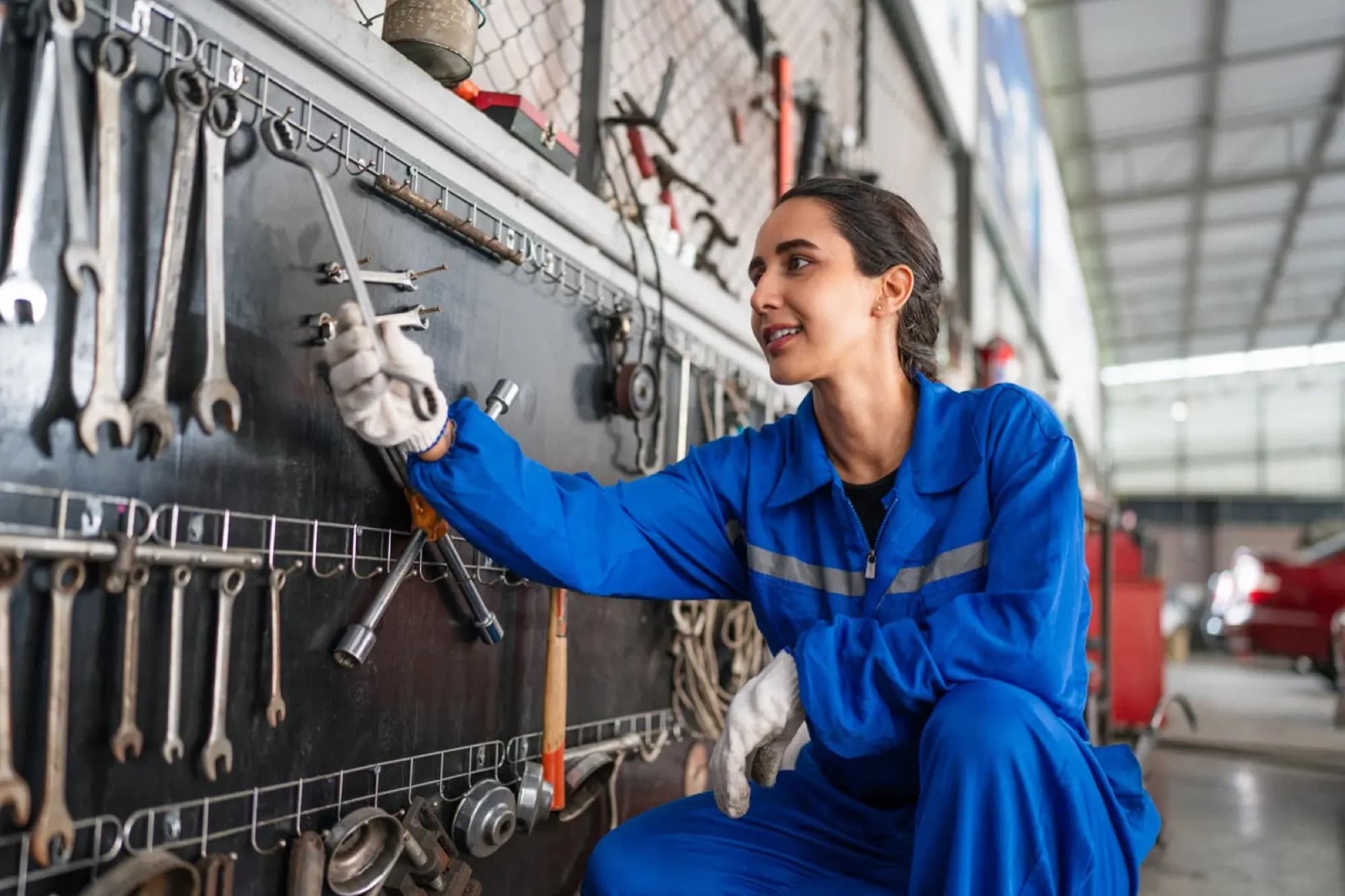 Technicienne en combinaison bleue prenant une clé sur le panneau d'outillage mural d'un atelier