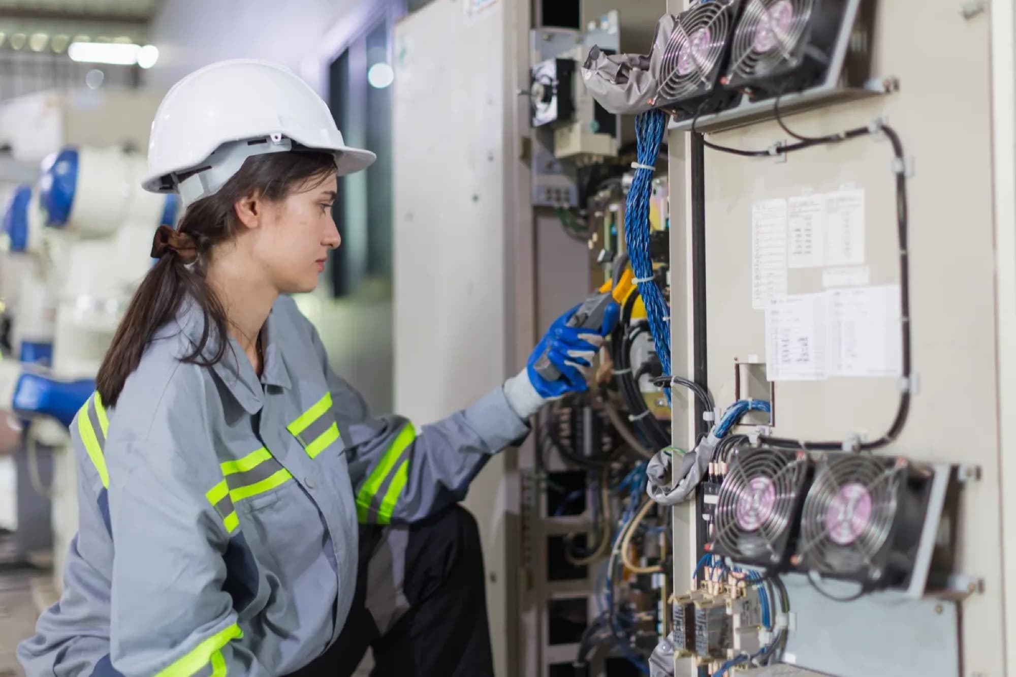 Technicienne intervenant à la pince sur le câblage d'une armoire de commande ventilée, robots en arrière-plan