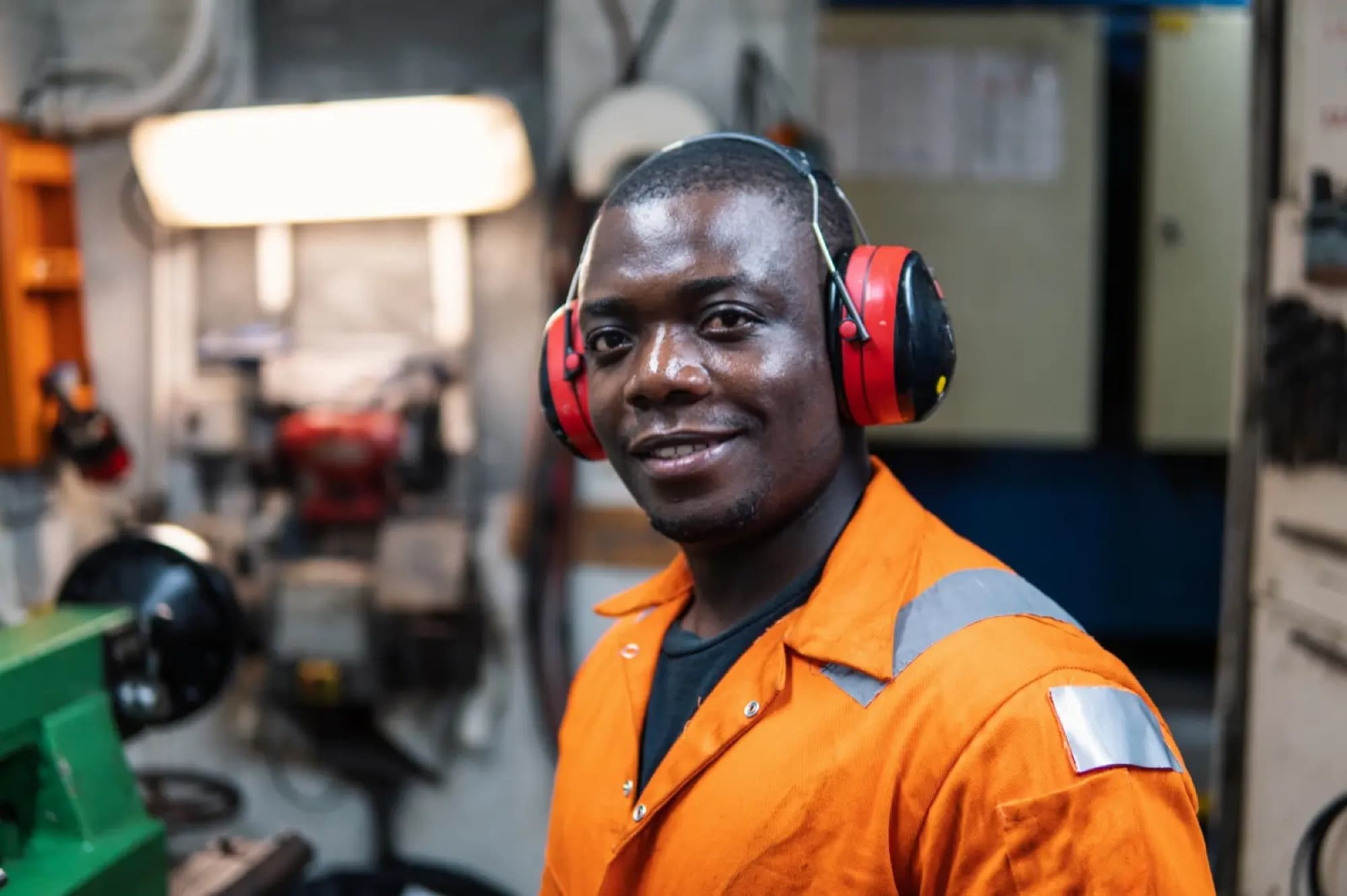 Technicien en combinaison orange et casque antibruit dans un atelier d'usinage équipé d'un étau et de machines
