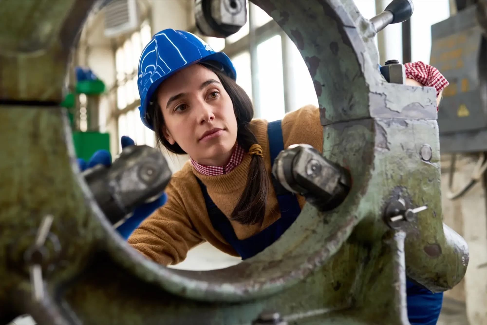 Technicienne en casque bleu inspectant l'intérieur d'un corps de machine en fonte posé dans un atelier