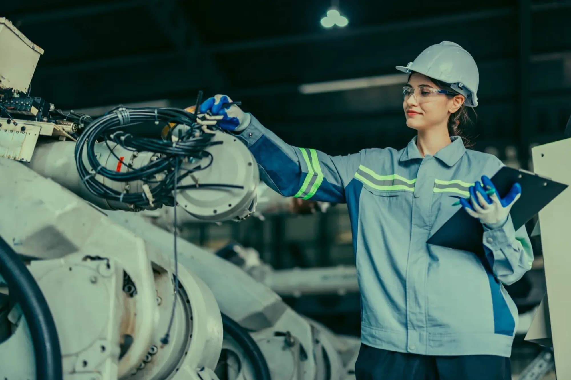 Technicienne, presse-papiers en main, inspectant le bras d'un robot industriel dans une halle de production