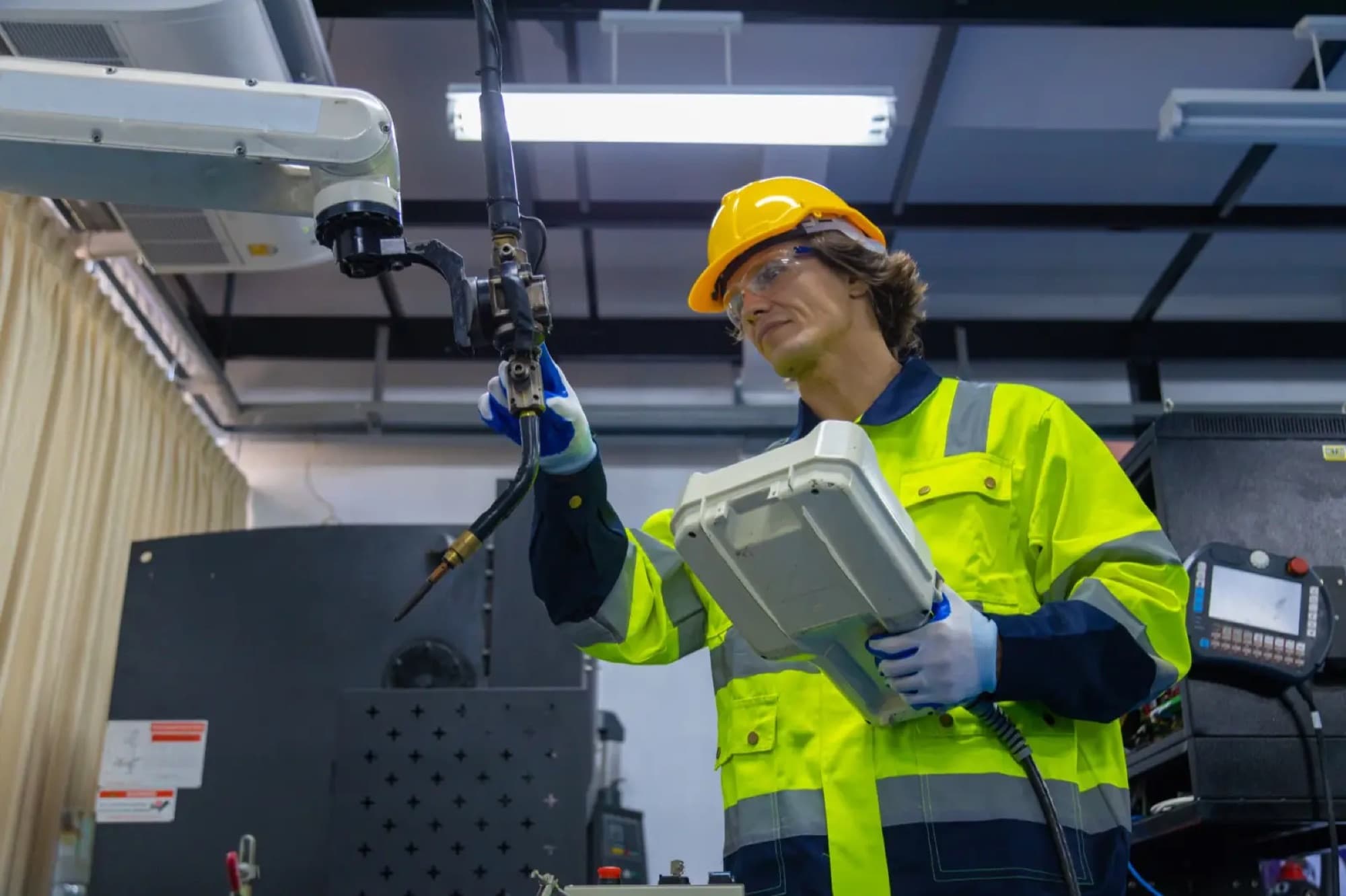 Technicien tenant un boîtier de programmation devant la torche de soudage portée par un robot
