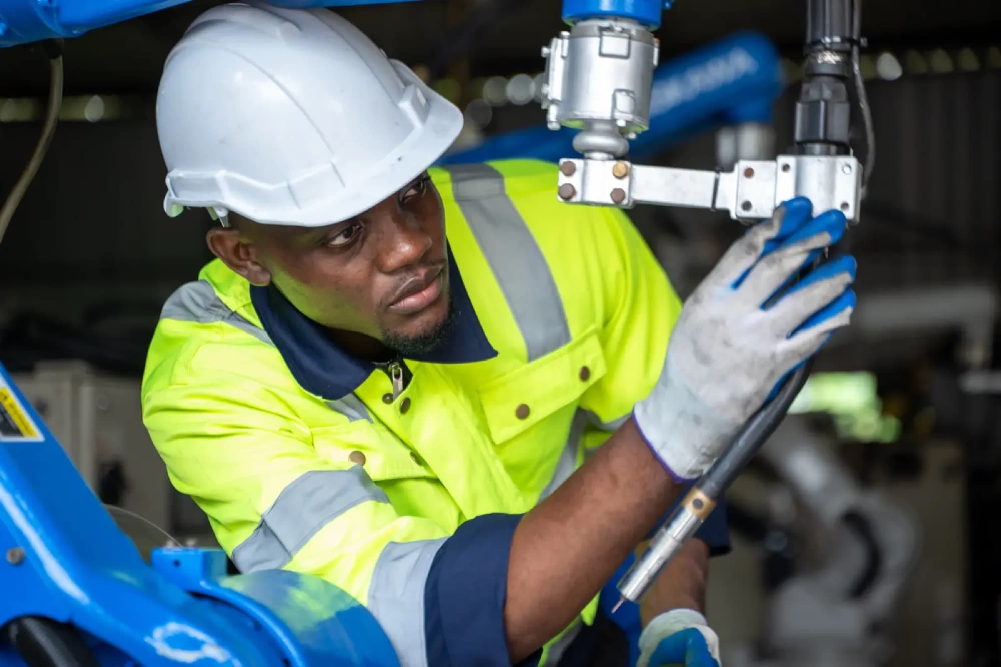 Technicien en casque blanc ajustant l'outil en bout de bras d'un robot industriel bleu
