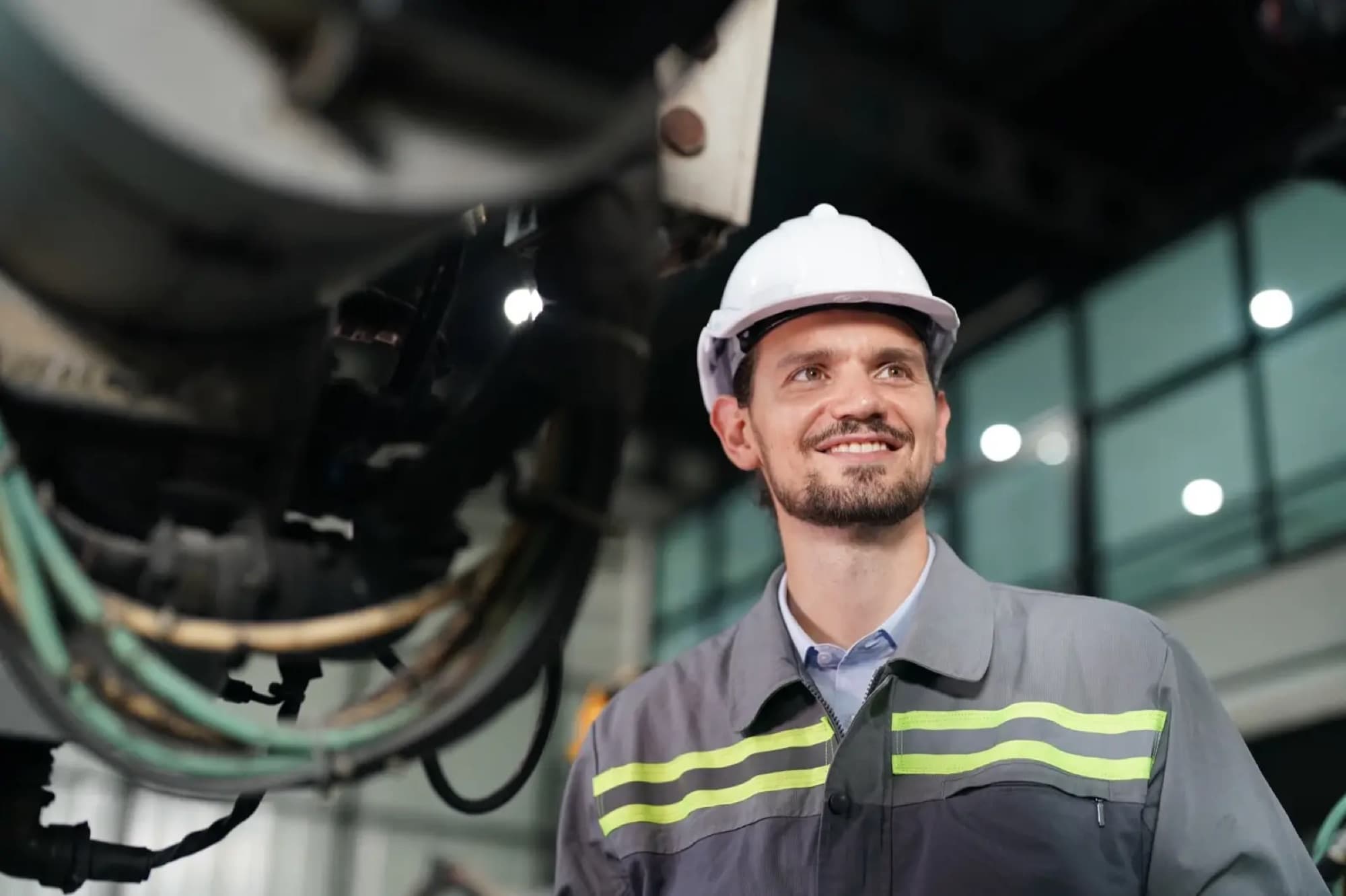 Technicien en casque blanc levant les yeux vers une machine suspendue dans une halle de production vitrée