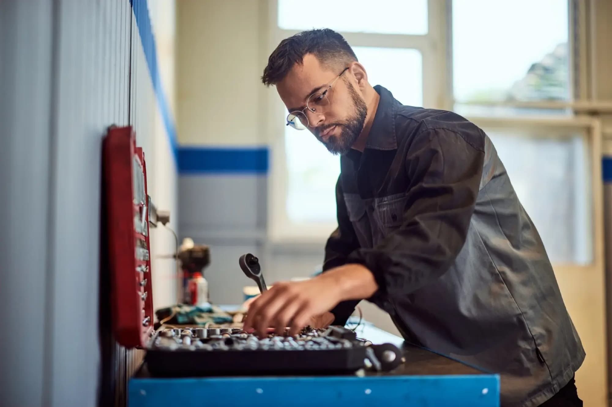 Technicien choisissant une douille dans le tiroir de sa servante à outils, cliquet en main