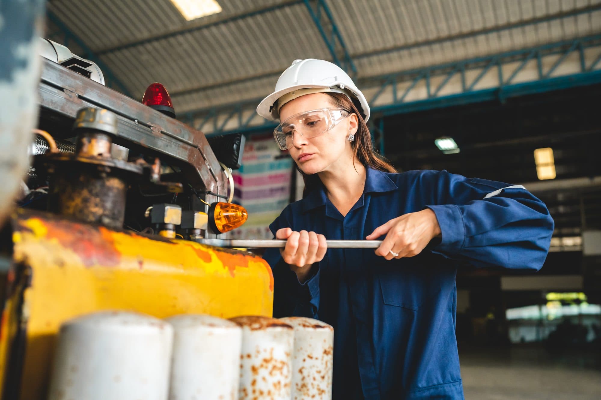 Technicienne serrant à la clé sur une machine en hall industriel